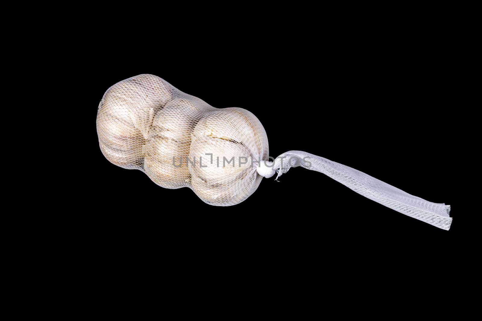 Packed garlic in a net isolated on a black background. Three garlic bulbs in a white net. Close-up
