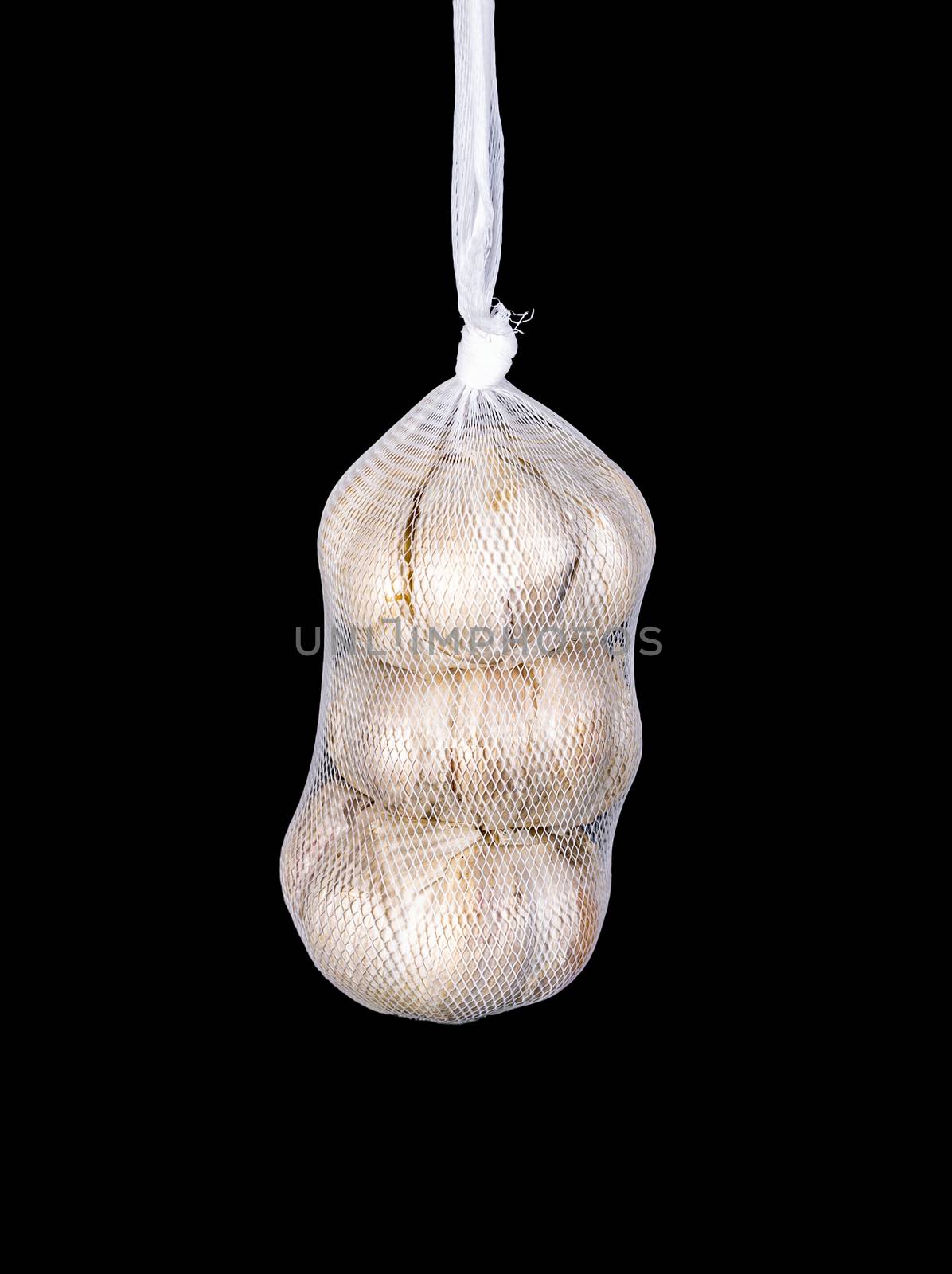 Packed garlic in a net isolated on a black background. Close-up. Three garlic bulbs in a white net.