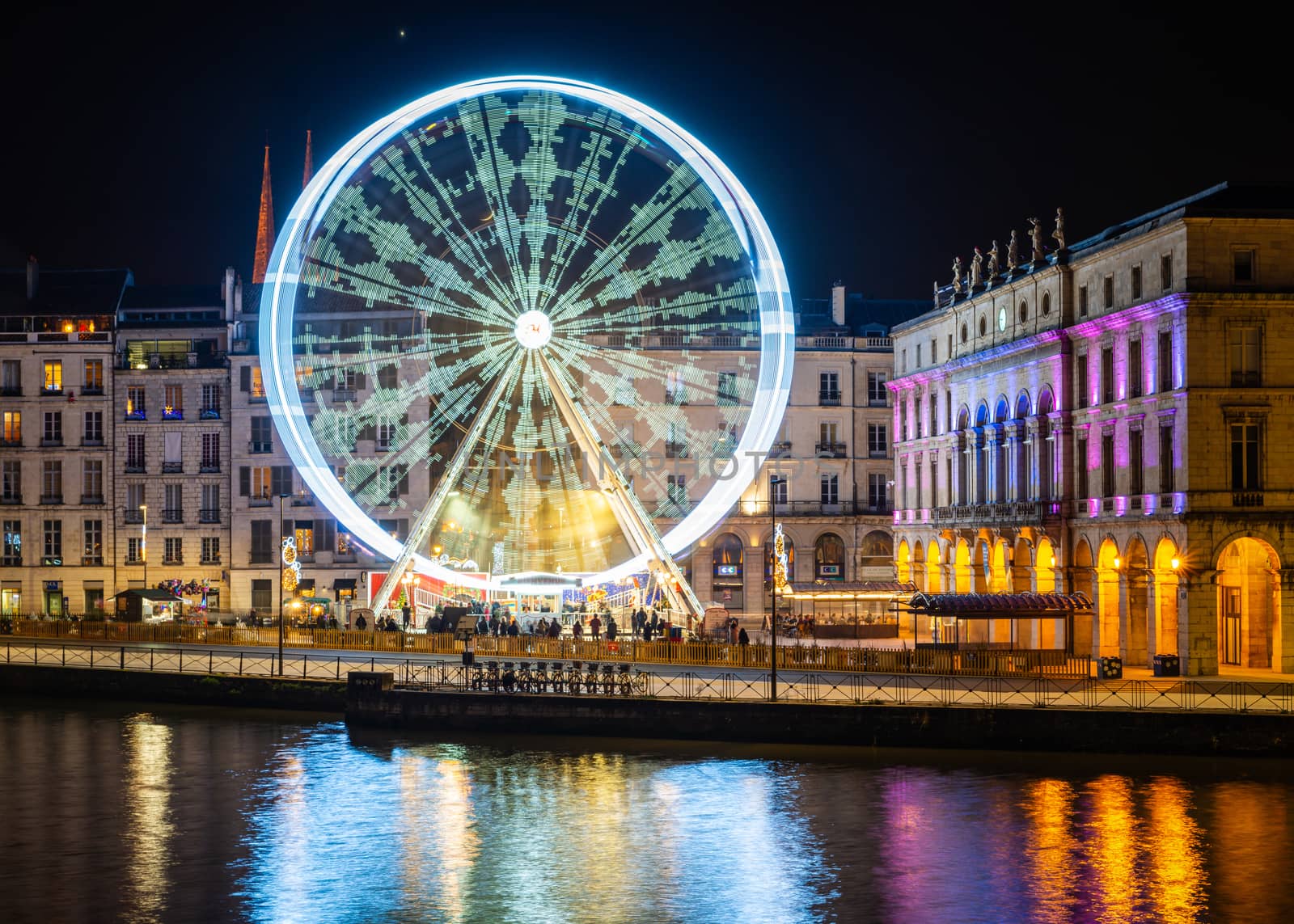 BAYONNE, FRANCE - DECEMBER 28, 2019: The ferris wheel at night. Bayonne city hall illuminated on the right hand side.