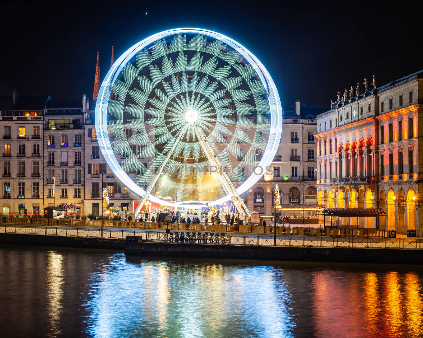 BAYONNE, FRANCE - DECEMBER 28, 2019: The ferris wheel at night. Bayonne city hall illuminated on the right hand side.