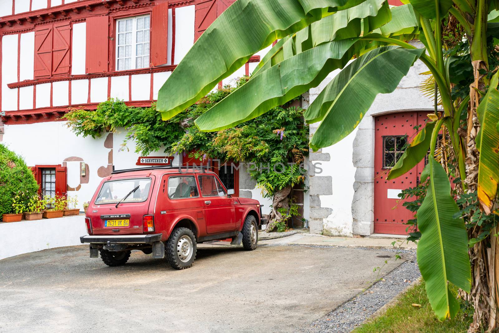 AINHOA, FRANCE - CIRCA JULY 2020: A red Lada 4x4 Niva parked in front of traditional white and red Basque house.