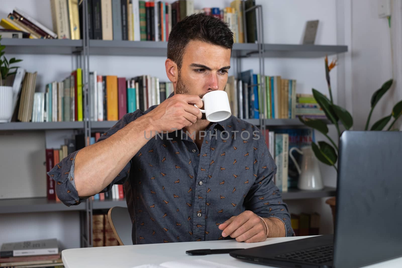 Handsome male businessman working on laptop and drinking tea from home