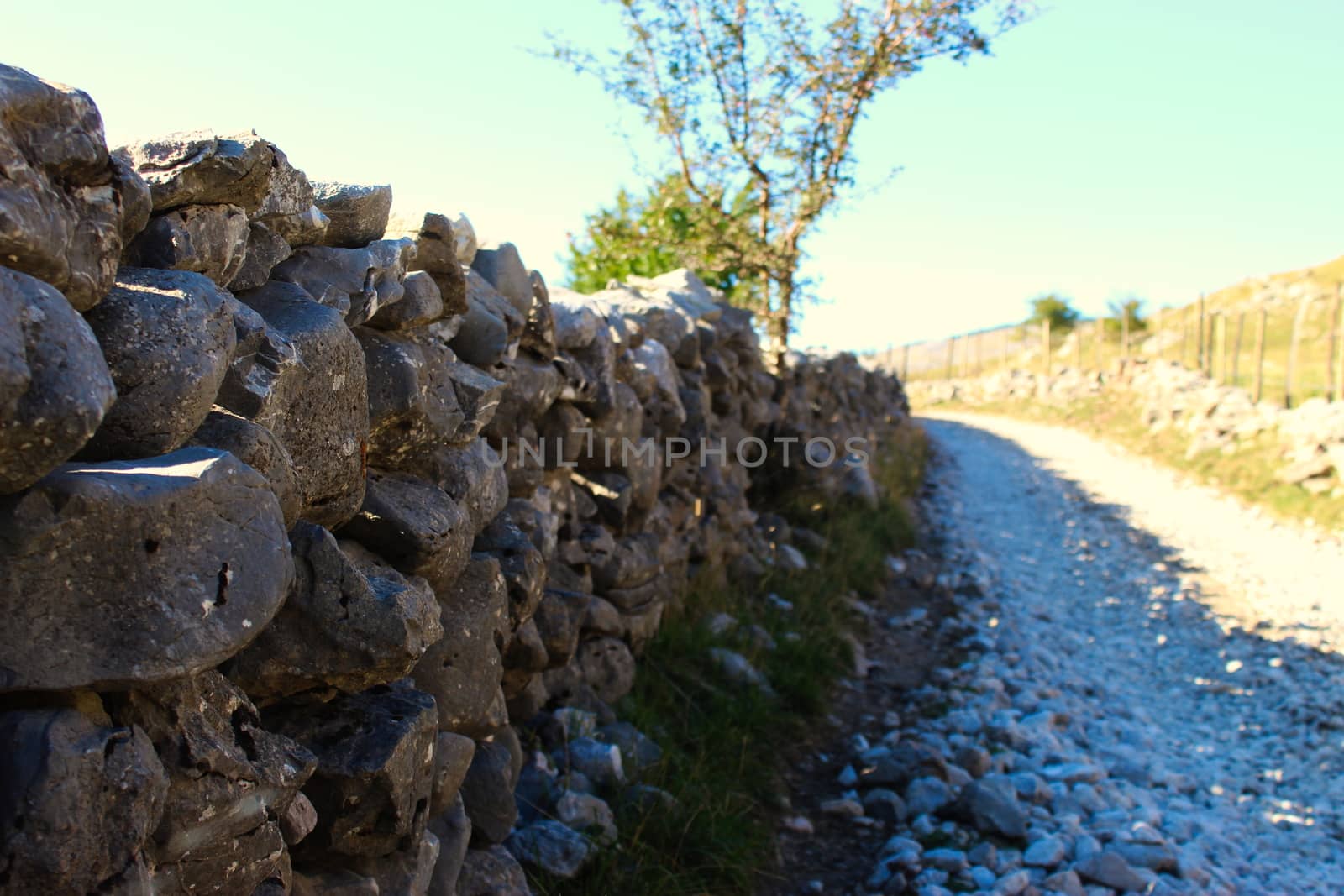 Large stones stacked in the wall to fence off the field from the road. Road to the old Bosnian village of Lukomir. by mahirrov