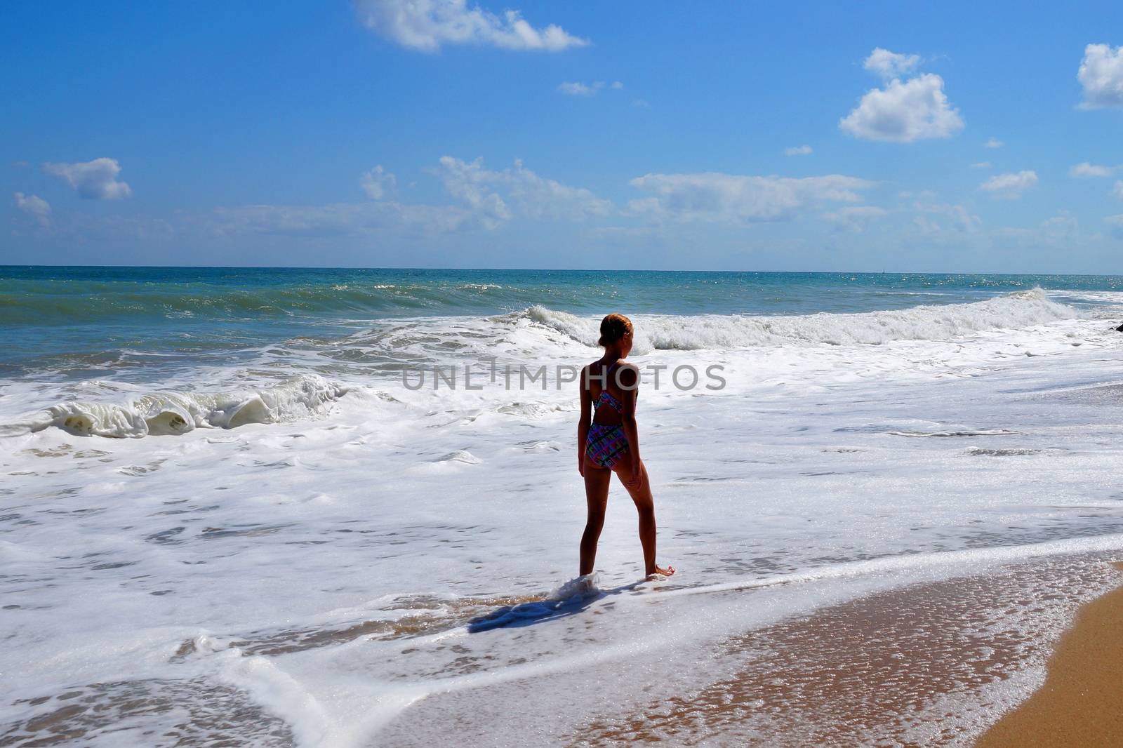 teenage girl walking alone along the empty seashore on the sunny day by Annado