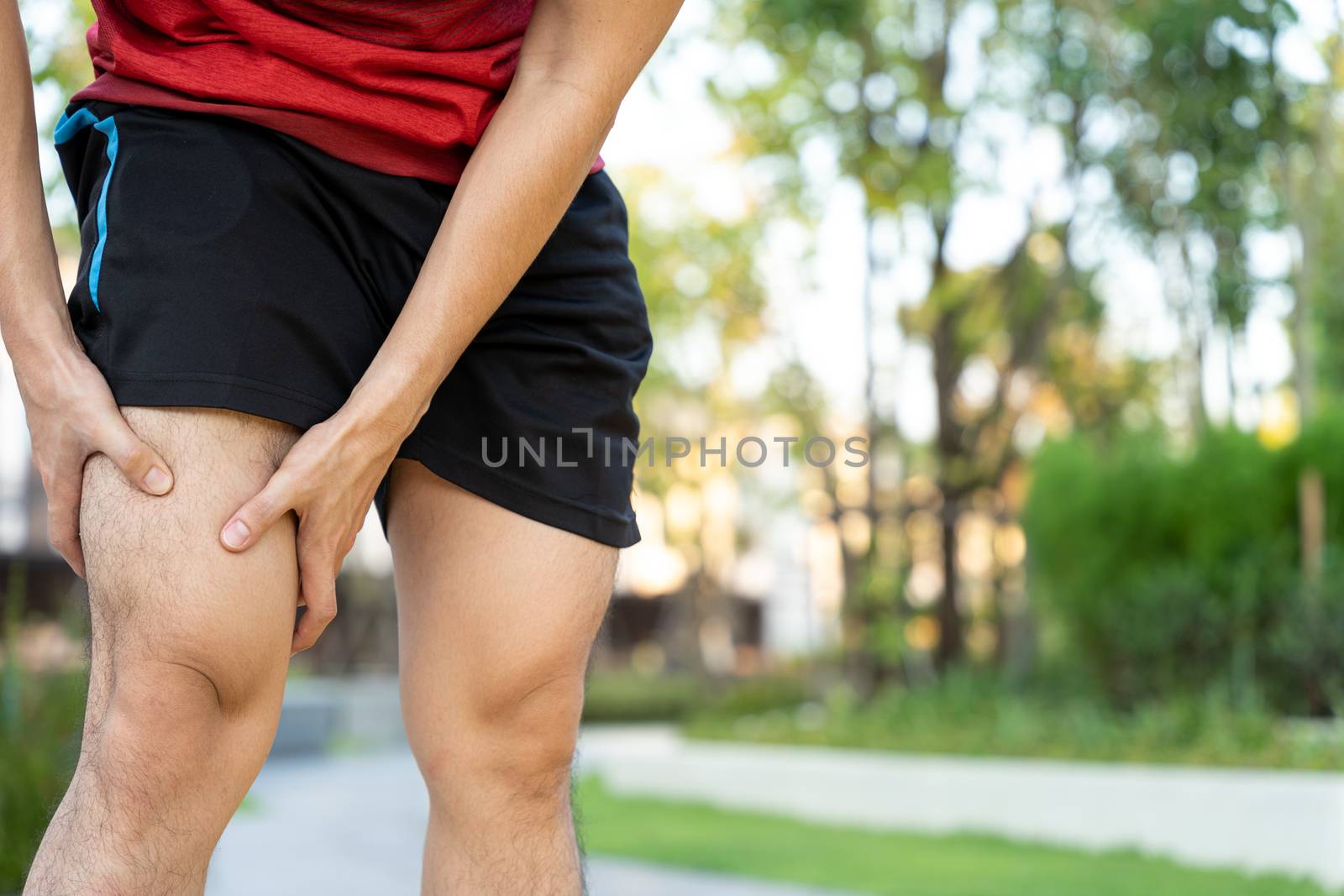 Male runner athlete leg injury and pain. Hands grab painful knee while running in the park. by mikesaran