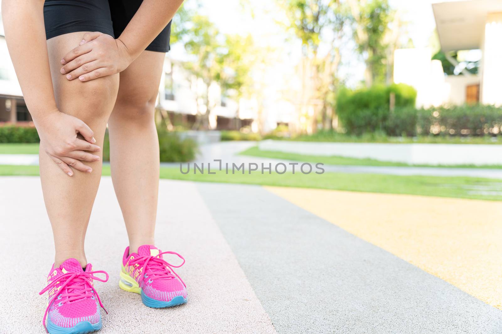 Female fatty runner athlete leg injury and pain. Hands grab painful knee while running in the park.