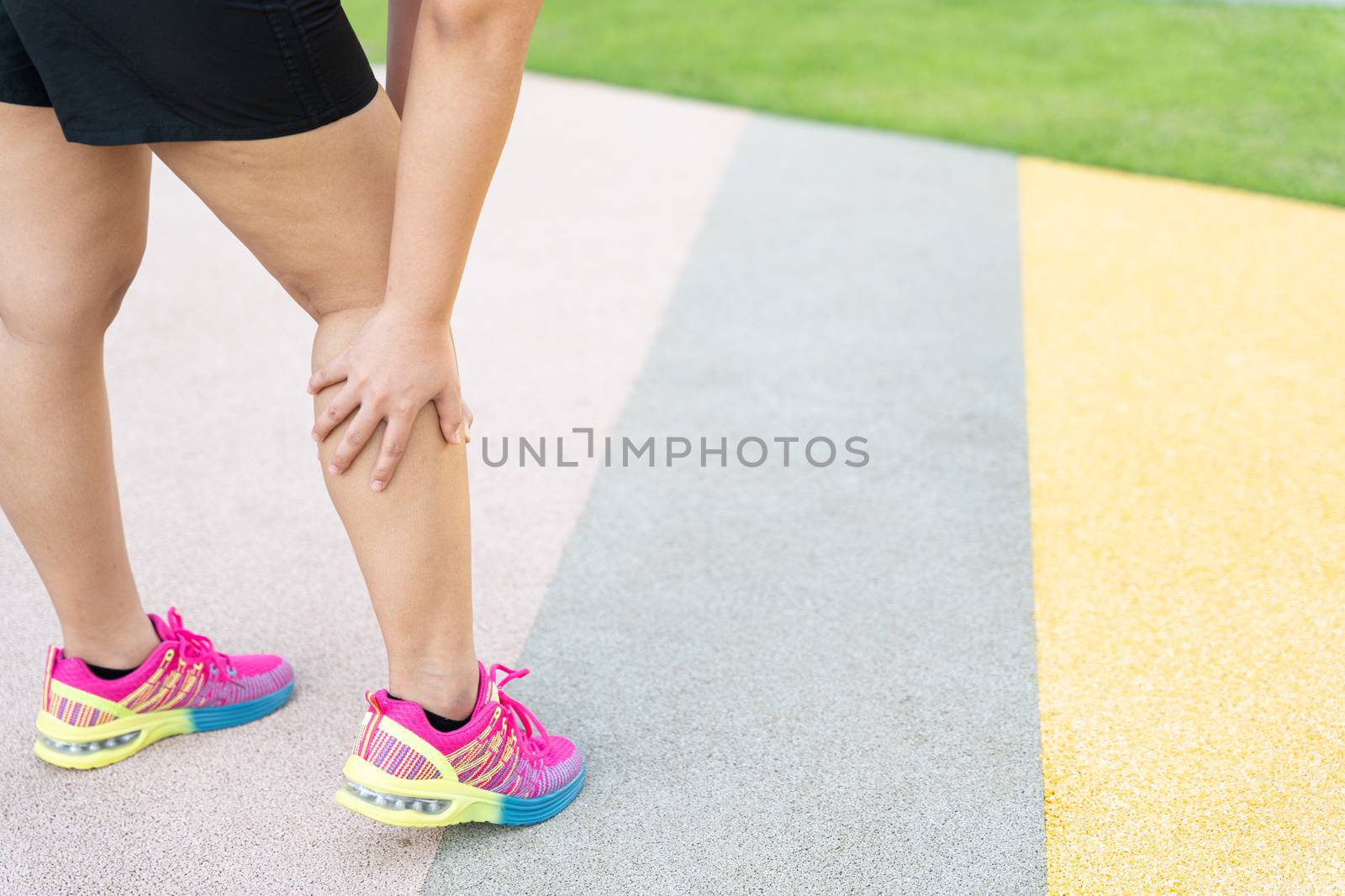 Female fatty runner athlete leg injury and pain. Hands grab painful leg while running in the park. by mikesaran