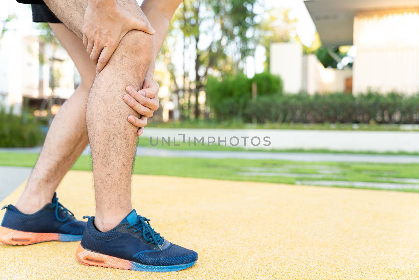 Male runner athlete leg injury and pain. Hands grab painful knee while running in the park.