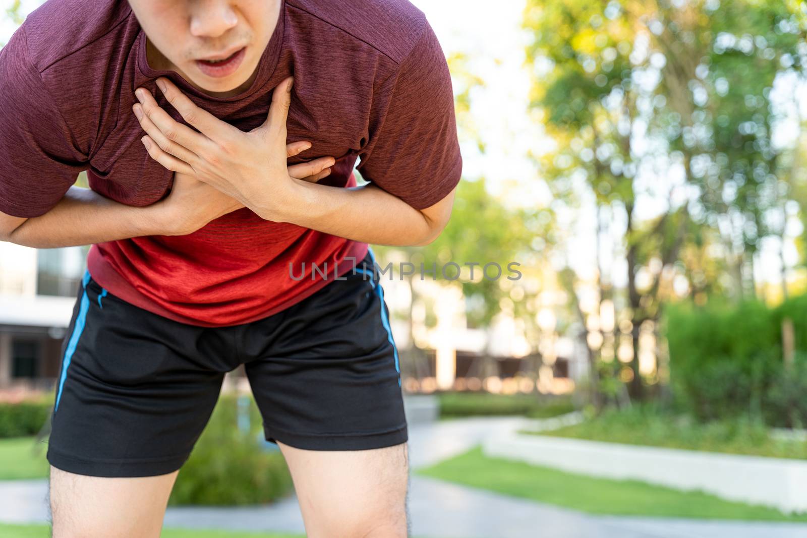 Exhausted male runner athlete suffering painful angina pectoris or asthma breathing problems while running in the park.