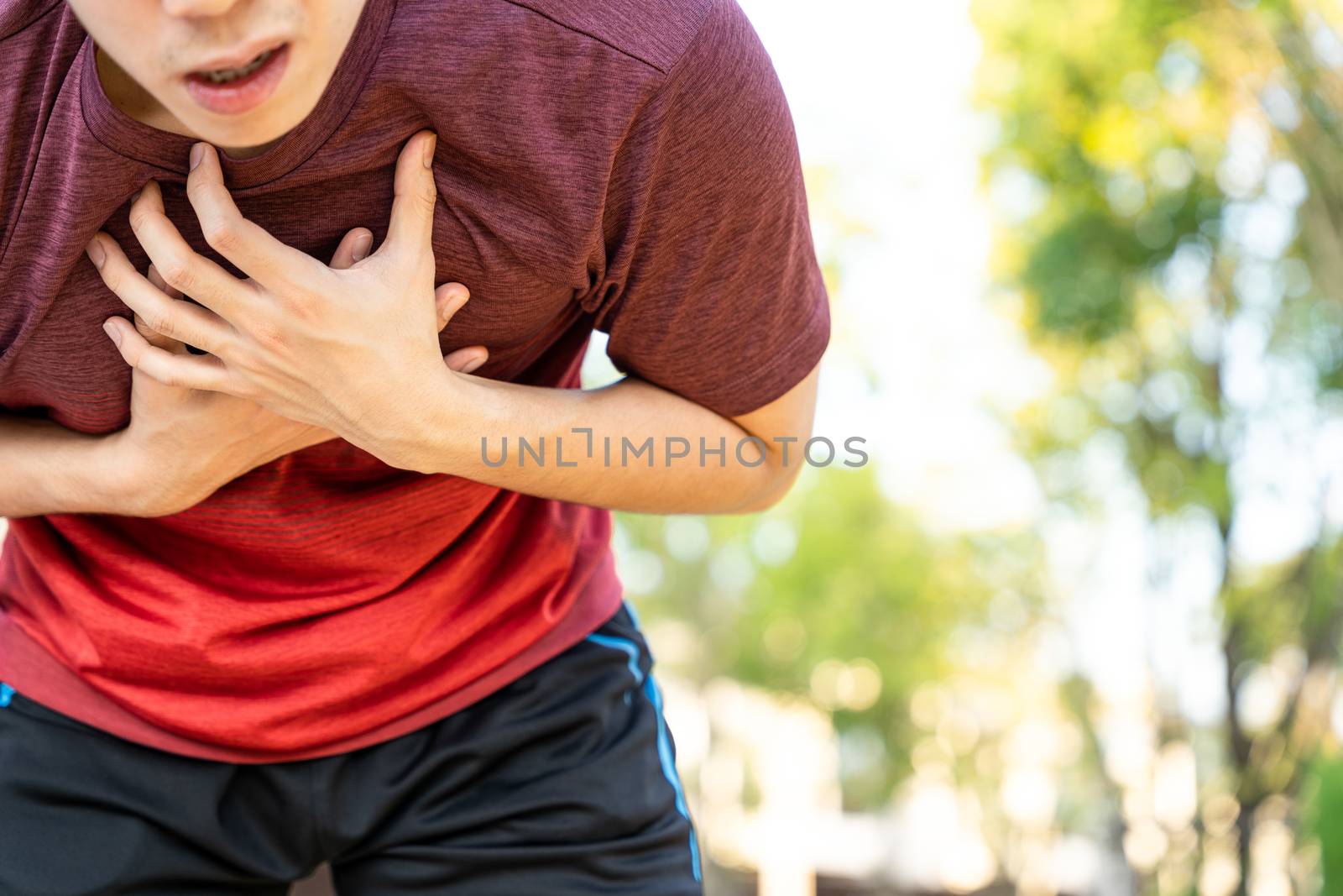 Exhausted male runner athlete suffering painful angina pectoris or asthma breathing problems while running in the park. by mikesaran