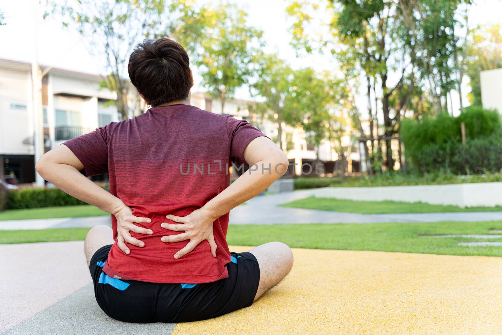 Male athlete suffering from back pain and injury. Hands grab back or waist after running in the park. by mikesaran