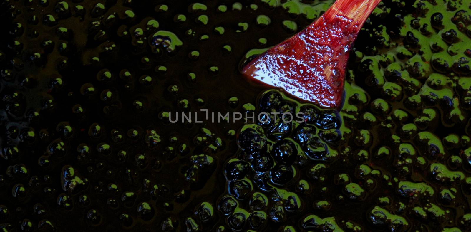 Banner. Top-down view of chokeberry jam, on the surface of the berries with a wooden cooking spoon. by mahirrov