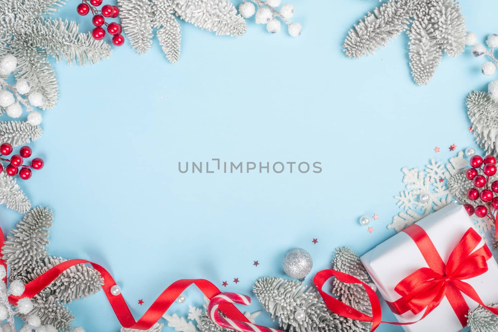 Frosted fir tree twigs and Christmas decorative bauble balls and gift with red ribbon on blue background with copy space for text template flat lay top view design