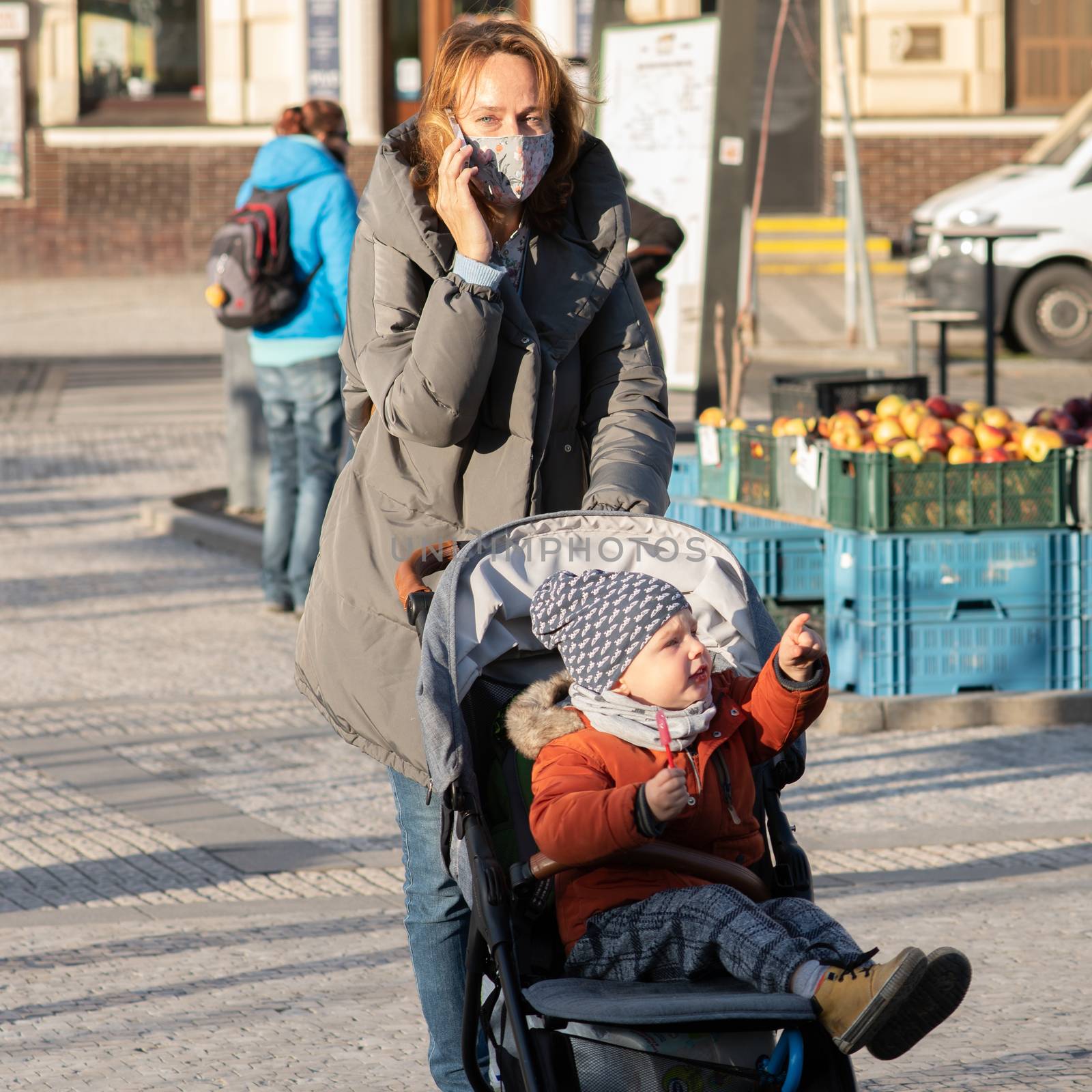 11/16/2020. Prague, Czech Republic. A mother is crossing the street with her small child in a baby carriage close to Hradcanska tram stop during quarantine. This is a lockdown period in the Czech Republic due to the increase of COVID-19 infectious in the country. Hradcanska tram stop it is in Prague 6