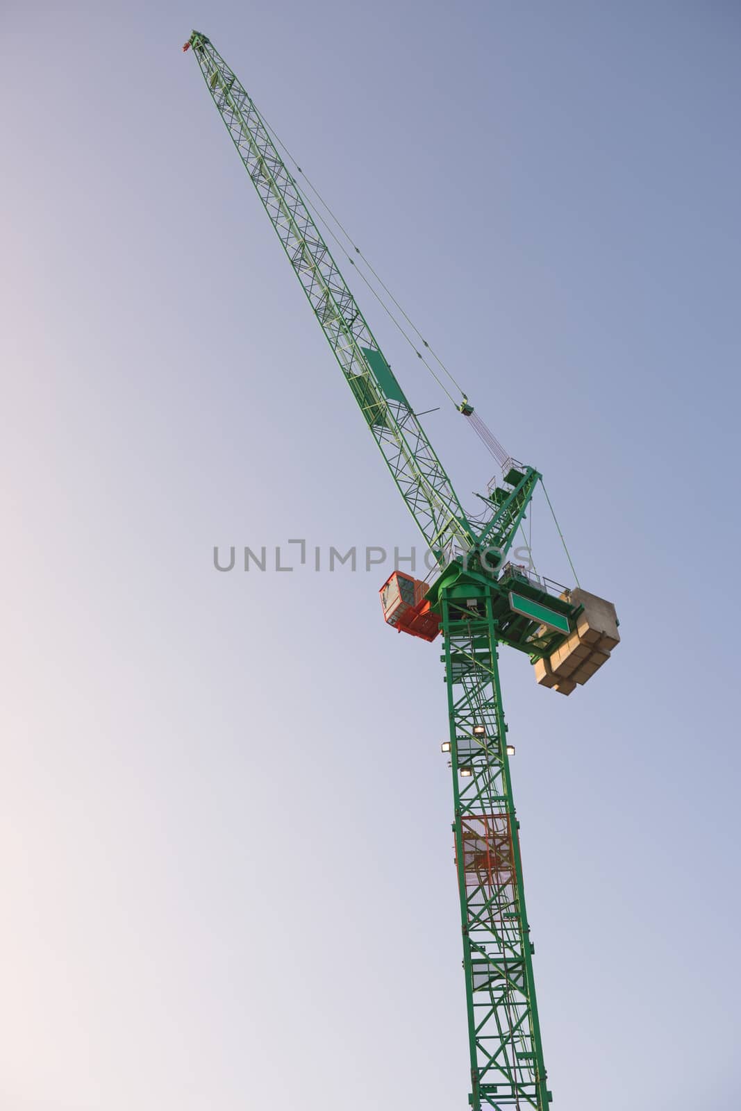 Top portion a tall tower crane at sunrise with a bright sky background. Modern construction machinery with fresh green and orange colors. metal frame.