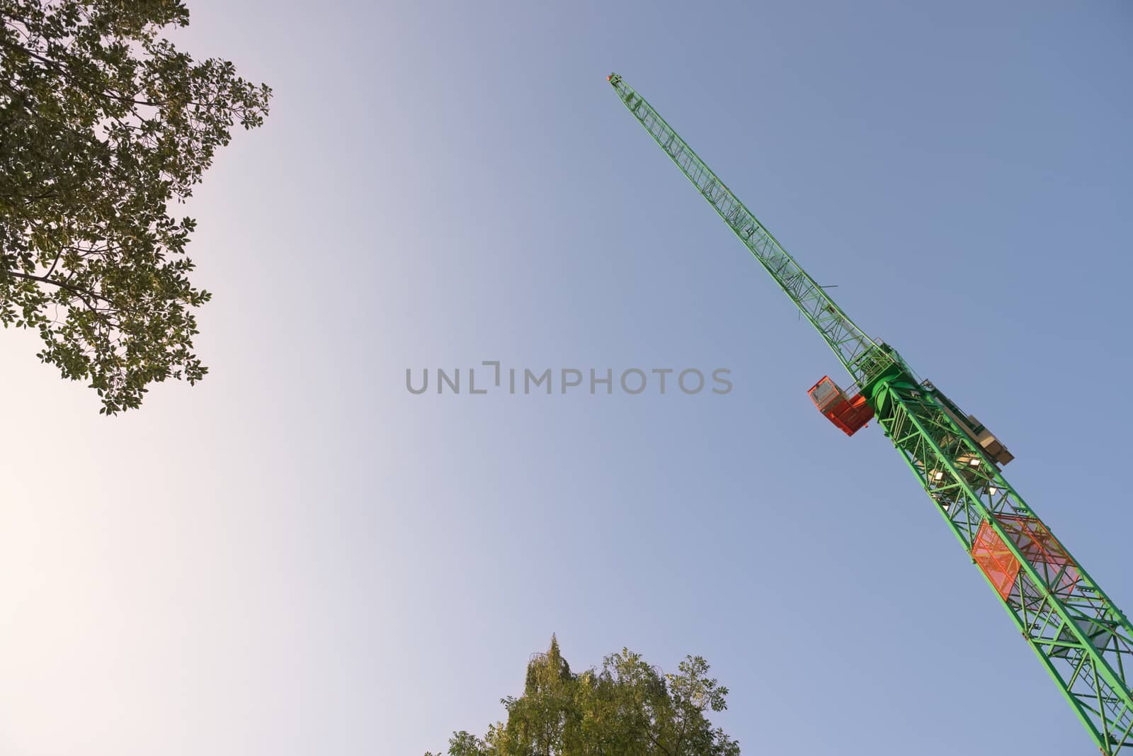 Smooth early morning sky background behind the leaves of tree tops and the leading jib of a large tower crane. Abstract with plenty of copy space.