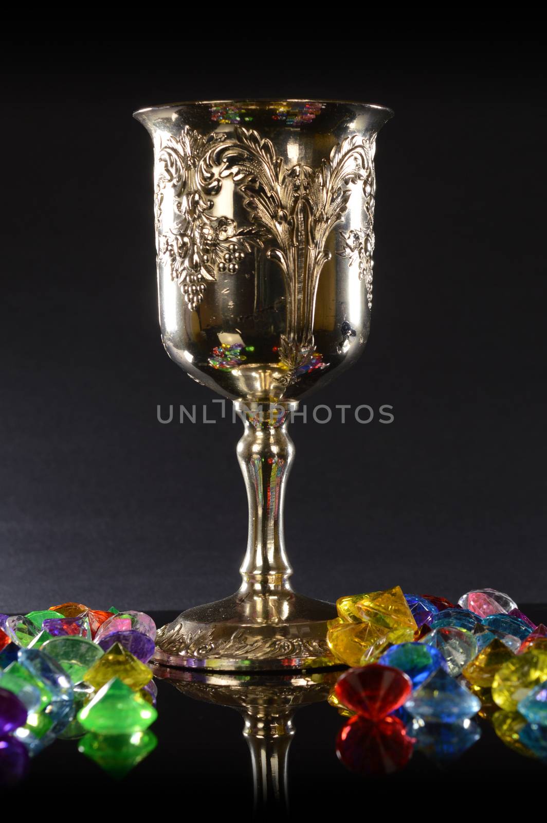 A silver wineglass with several pieces of gemstones over a black background.