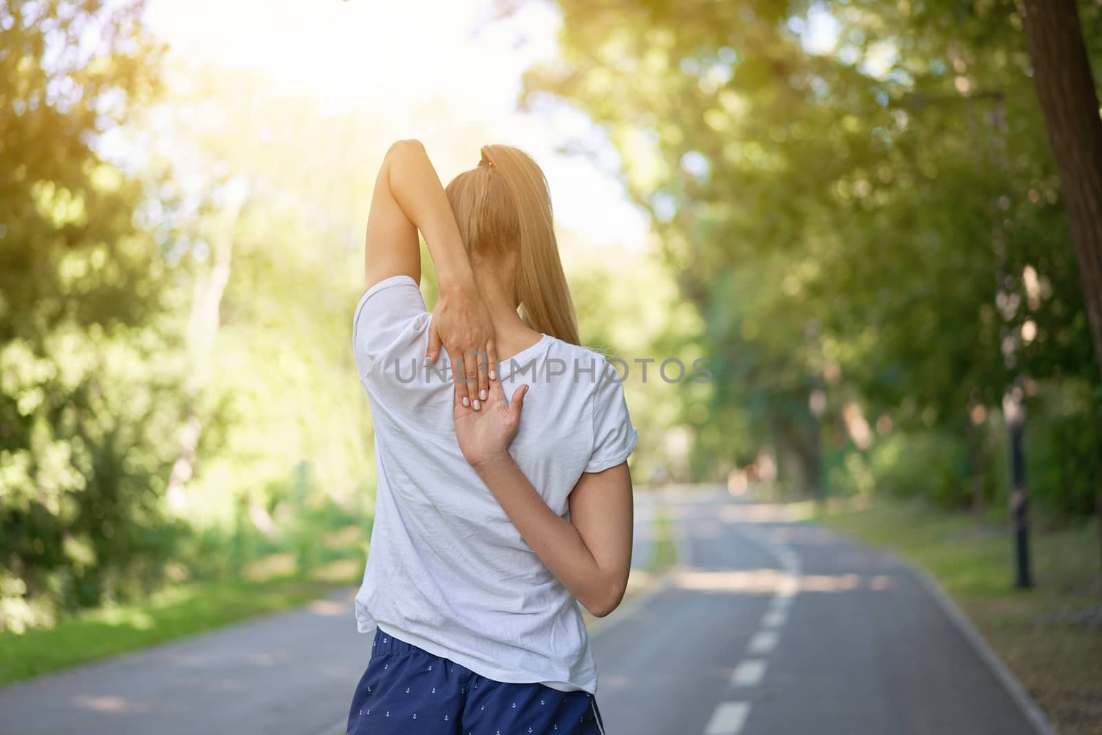 Woman runner stretching arms before exercising summer park morning Middle age athletic female warming up body before running Caucasian person warm up jogging Dressed white shirt shorts running track