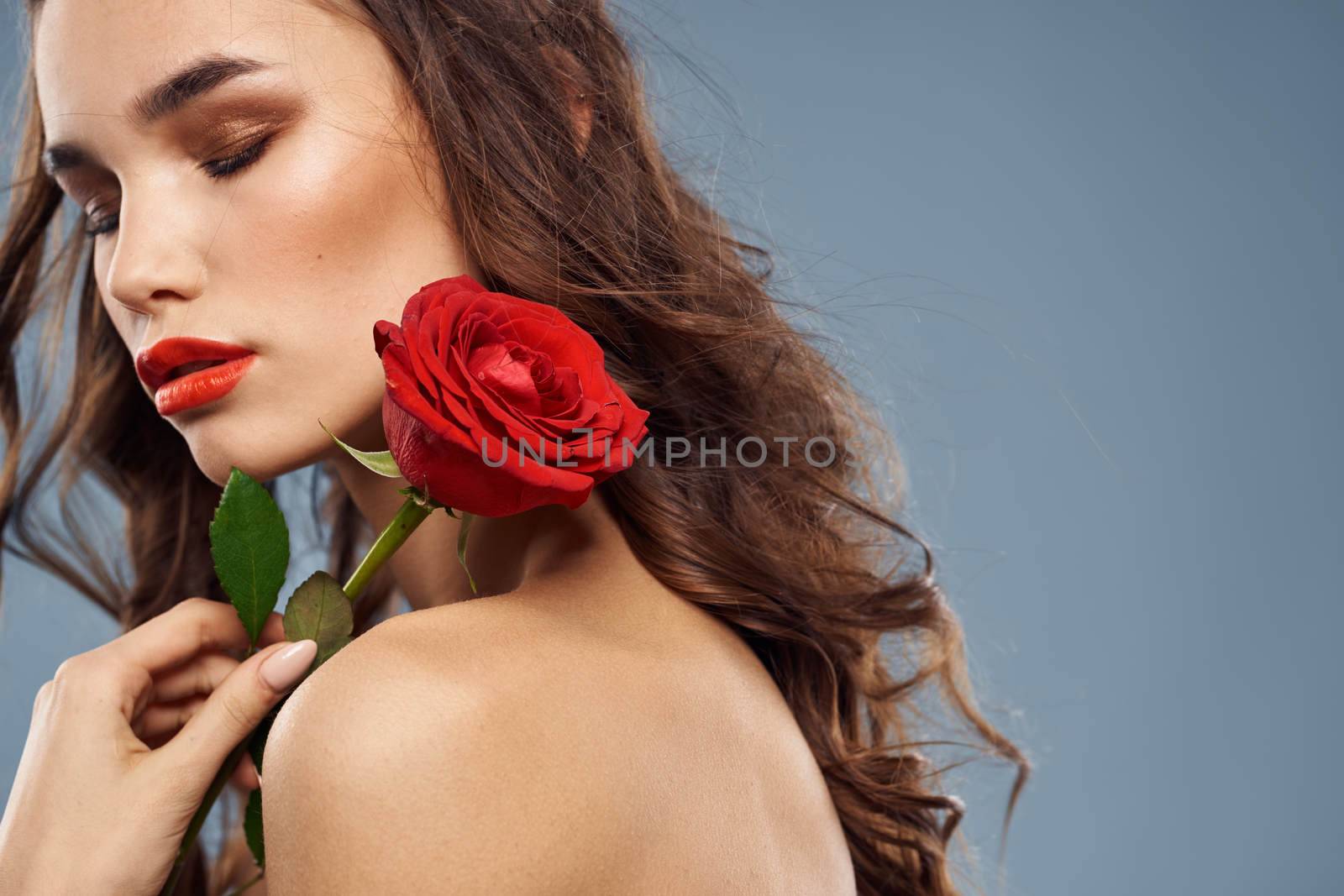 Portrait of a woman with a red rose in her hands on a gray background naked shoulders evening makeup. High quality photo
