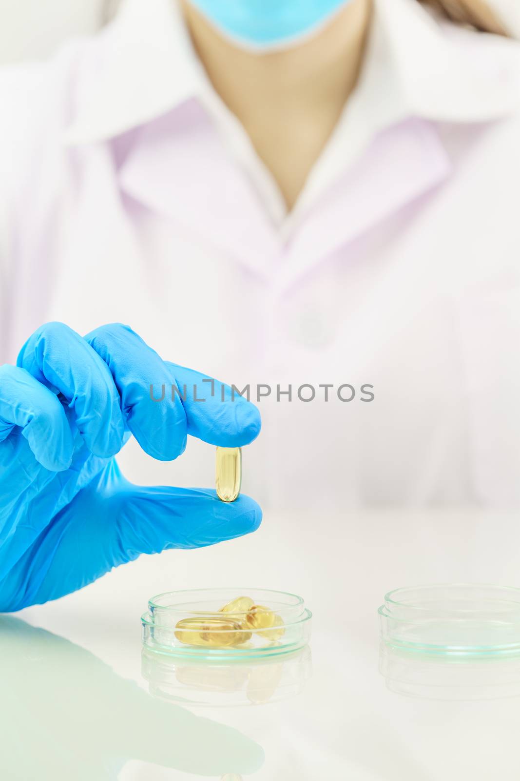 Close up Scientist hands putting in nitrile blue latex gloves holding Omega 3 capsule in labcoat wearing nitrile gloves, doing experiments in lab