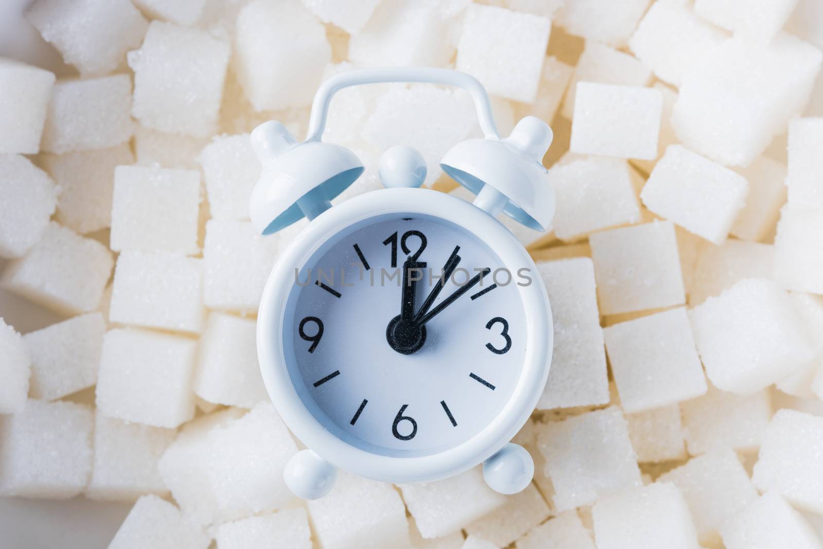 Sugar cube texture background sweet food ingredient and alarm clock, studio shot health high blood risk of diabetes, and calorie intake concept