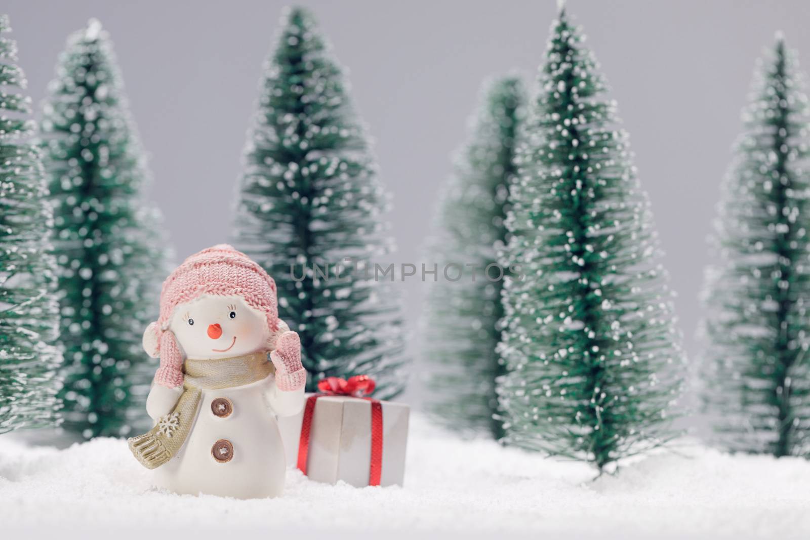 Small cute toy snowman with gift in forest in snow Christmas card design