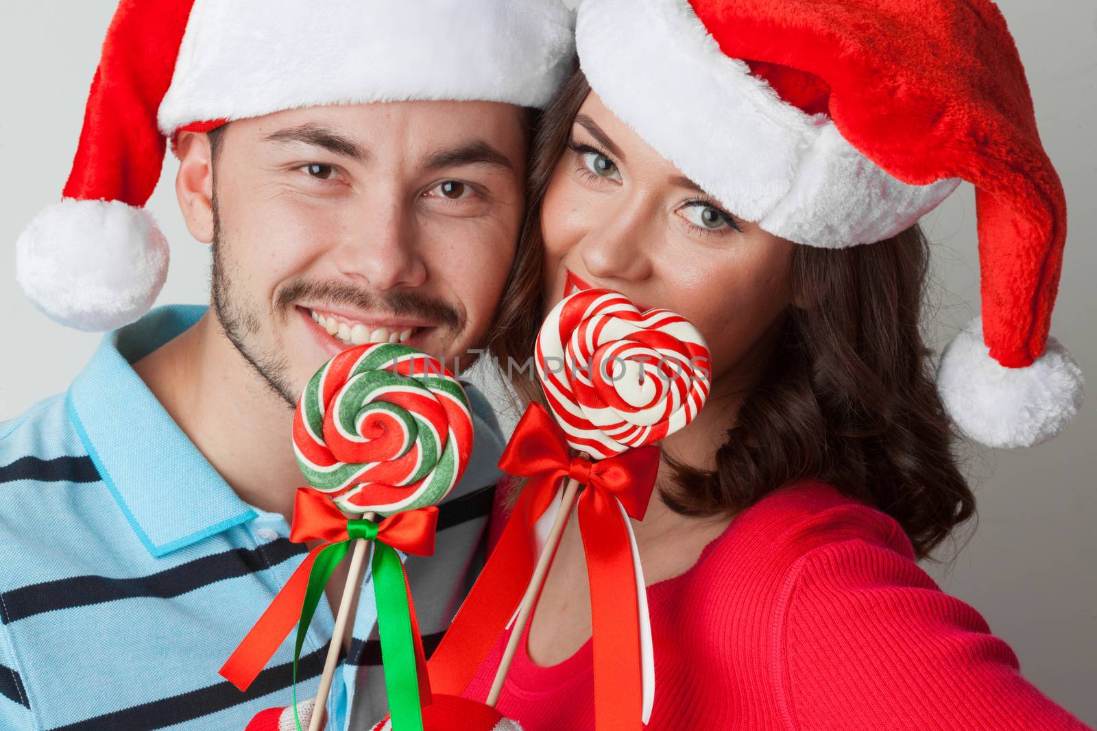 Young happy smiling couple in christmas santa hats with lollipops