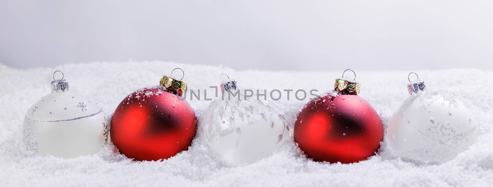 Christmas border of red and white baubles ornaments in snow on light background