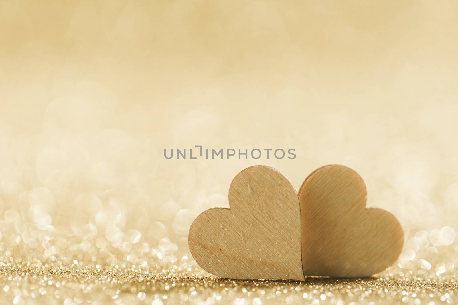 Two small handmade wooden hearts on bright golden lights bokeh background Valentines day card