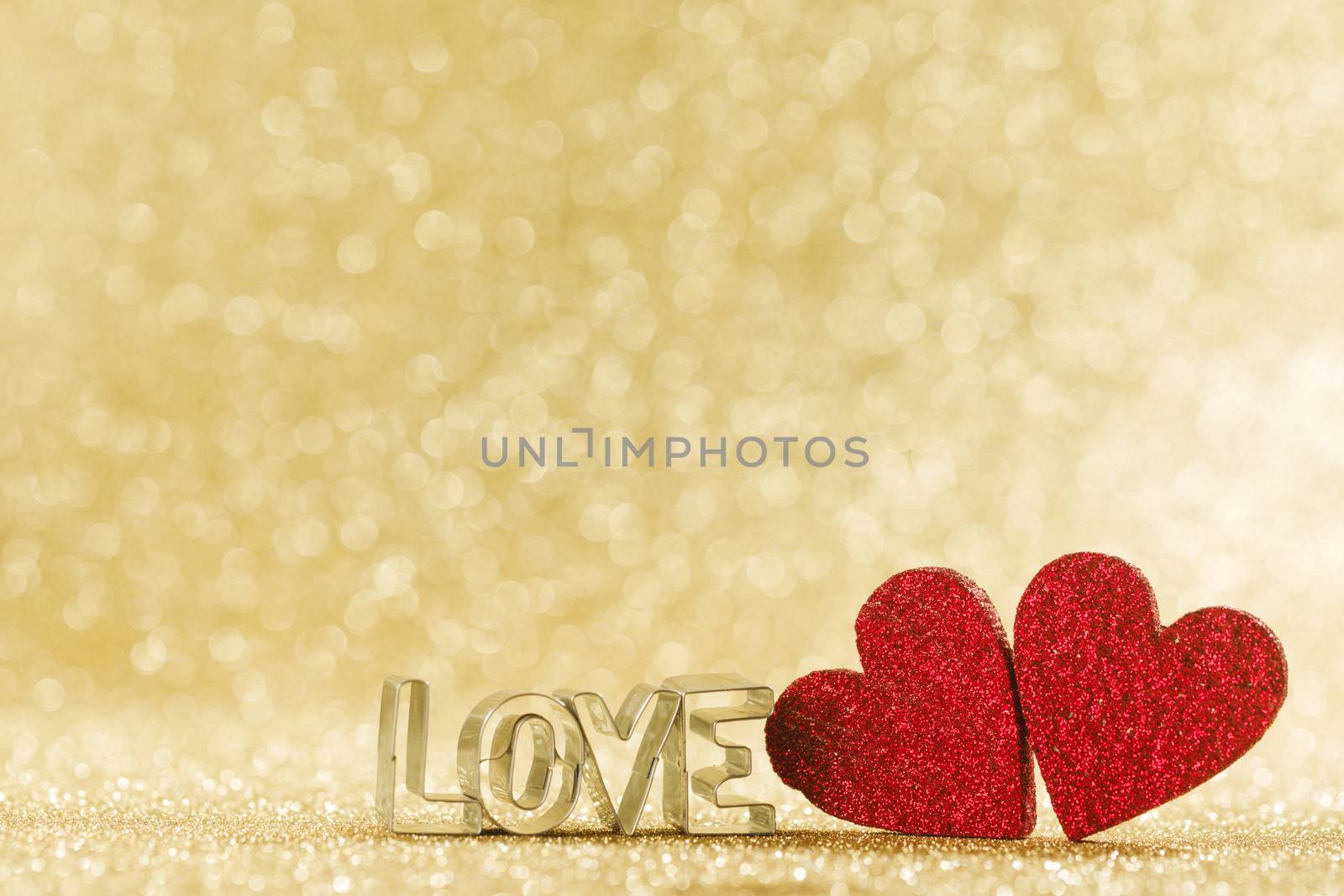 Two red handmade glitter hearts and word love on golden bright glitter lights bokeh background