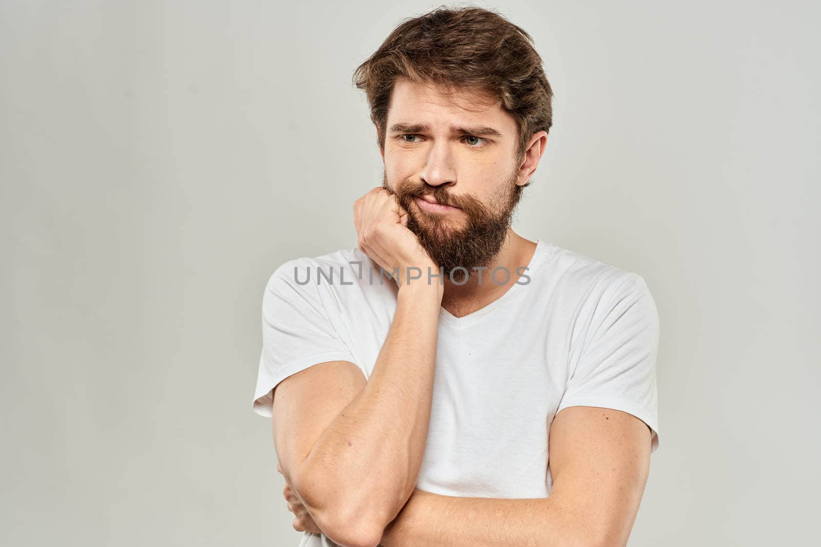 A man in a white t-shirt with a beard emotions displeased facial expression light background. High quality photo