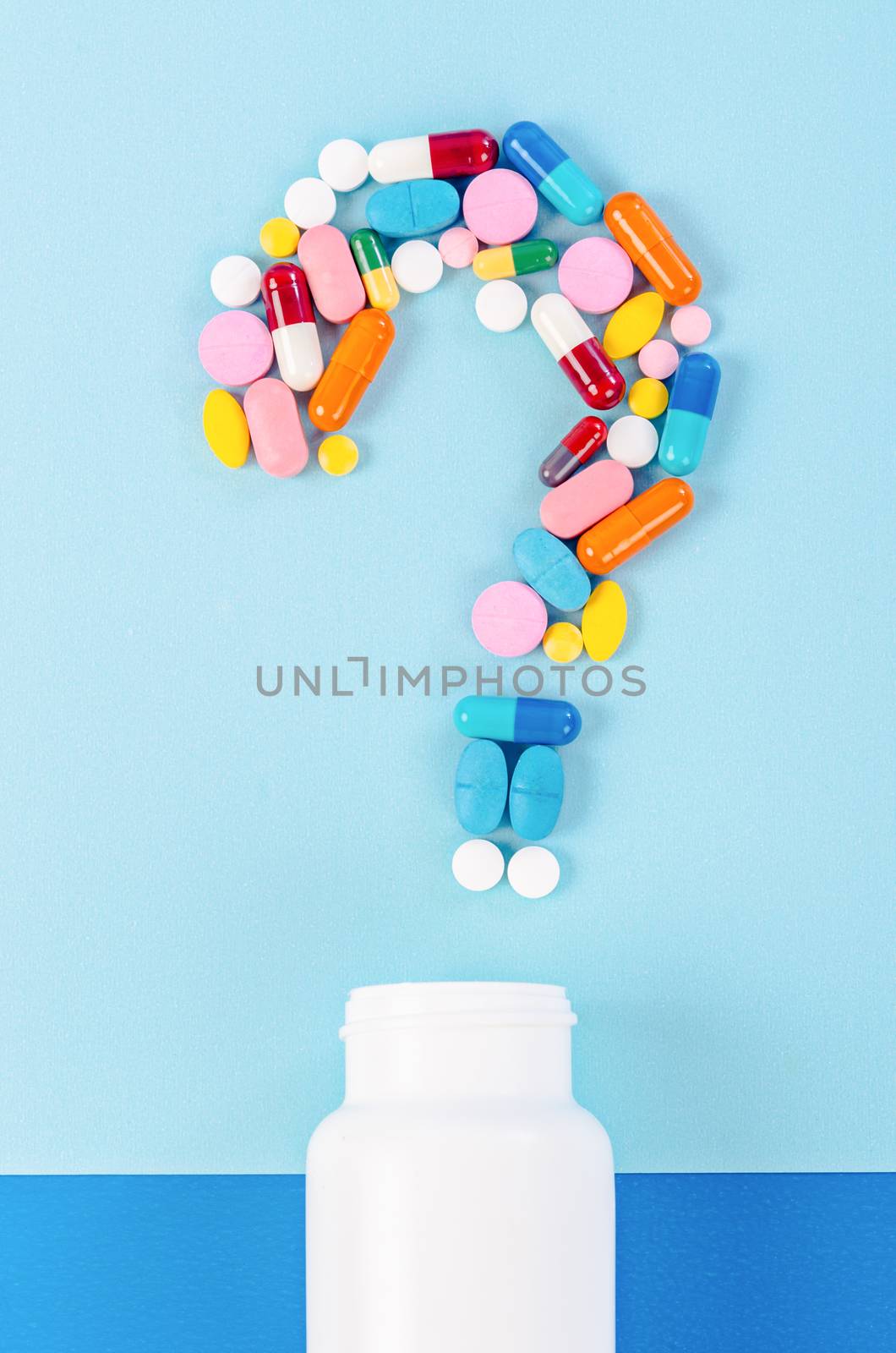 A question mark from laid out of medicine pills with bottle drug on blue background.
