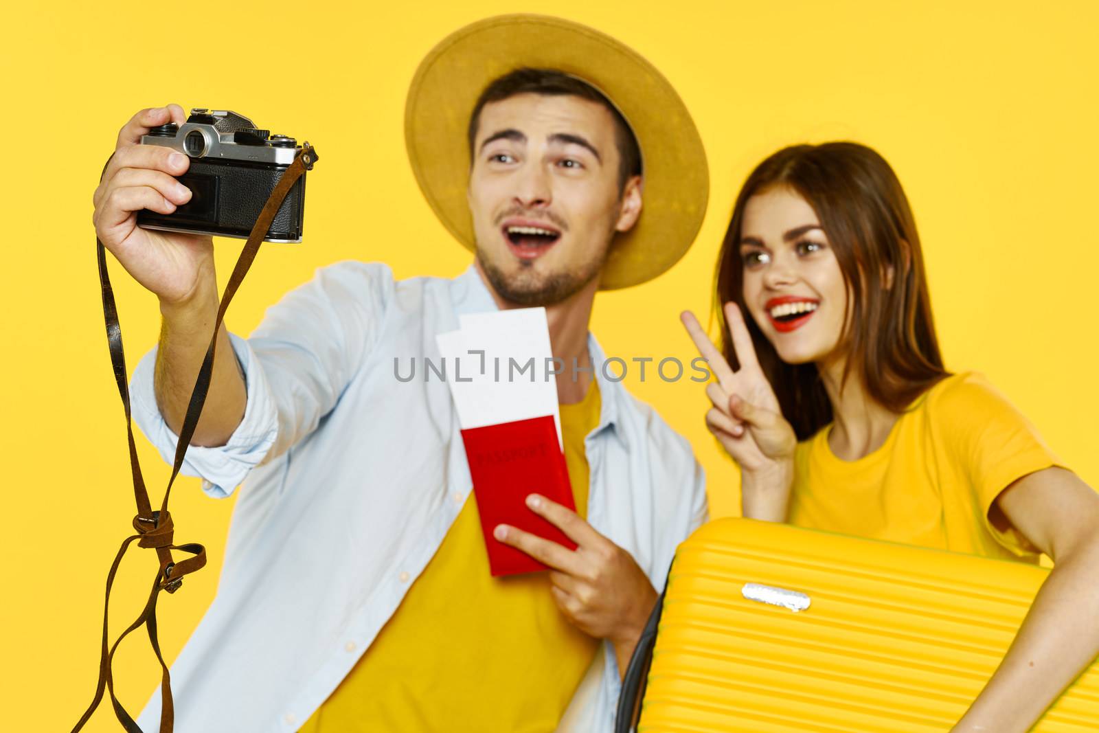 Young couple of travelers with passport and plane tickets holding camera smiling at the camera yellow suitcase