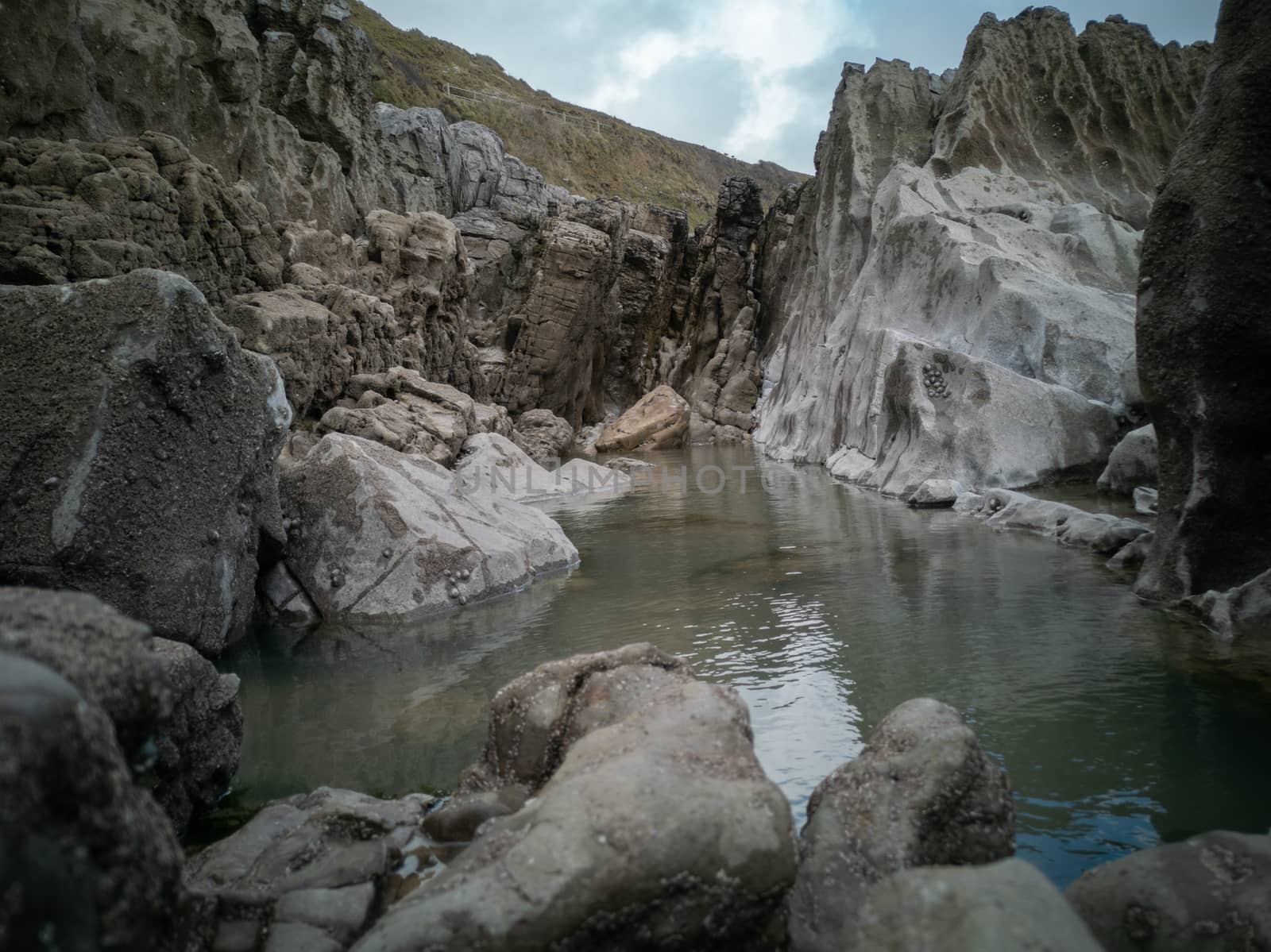 A large rock pool sitting between the tides with smooth rocks from sea erosion. Location: Caswell Bay, Gower, Wales, UK by WCLUK