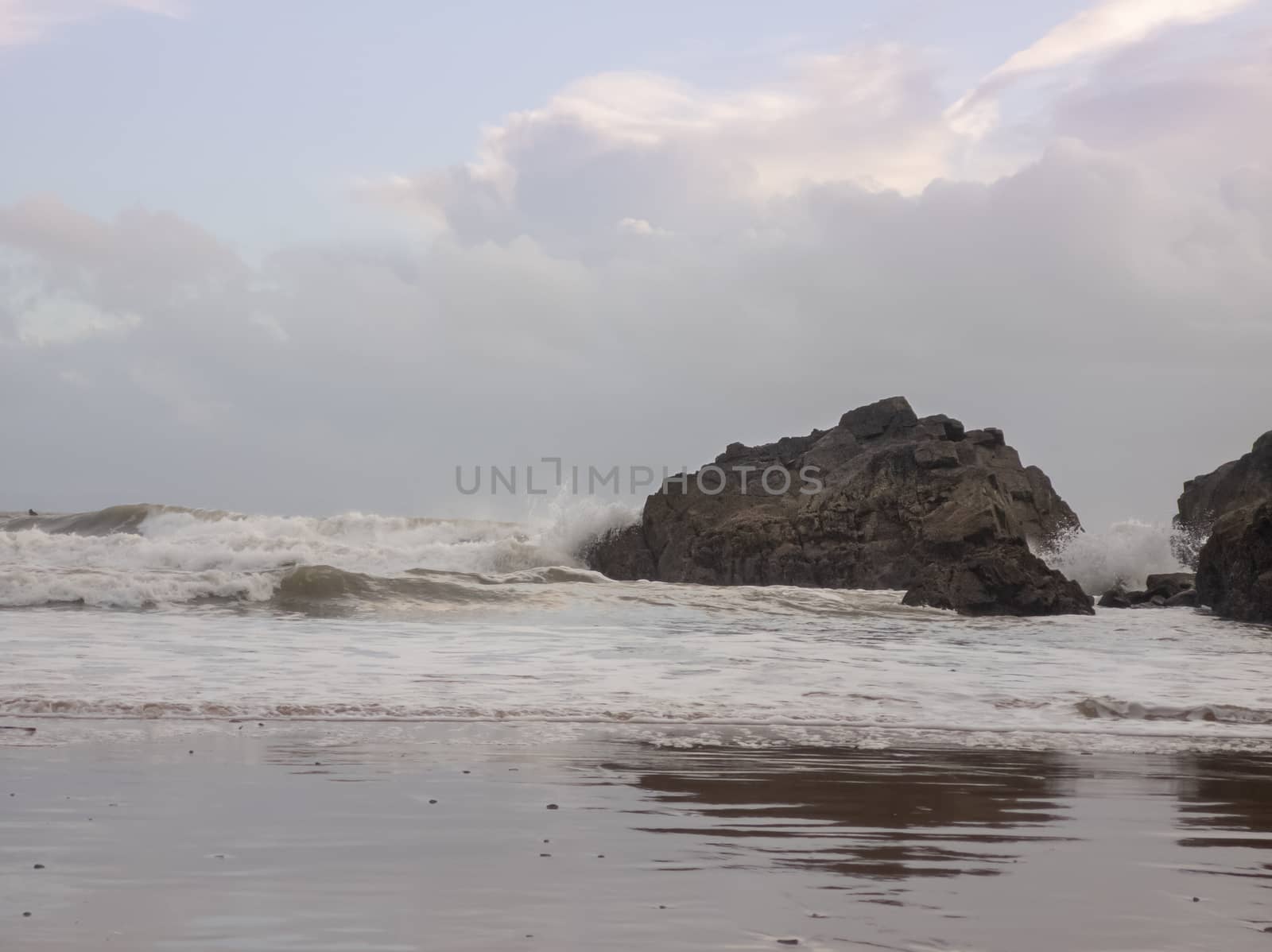 Waves crashing against a large rock as the tide moves in on Caswell Bay Beach, in Gower, Wales, UK.