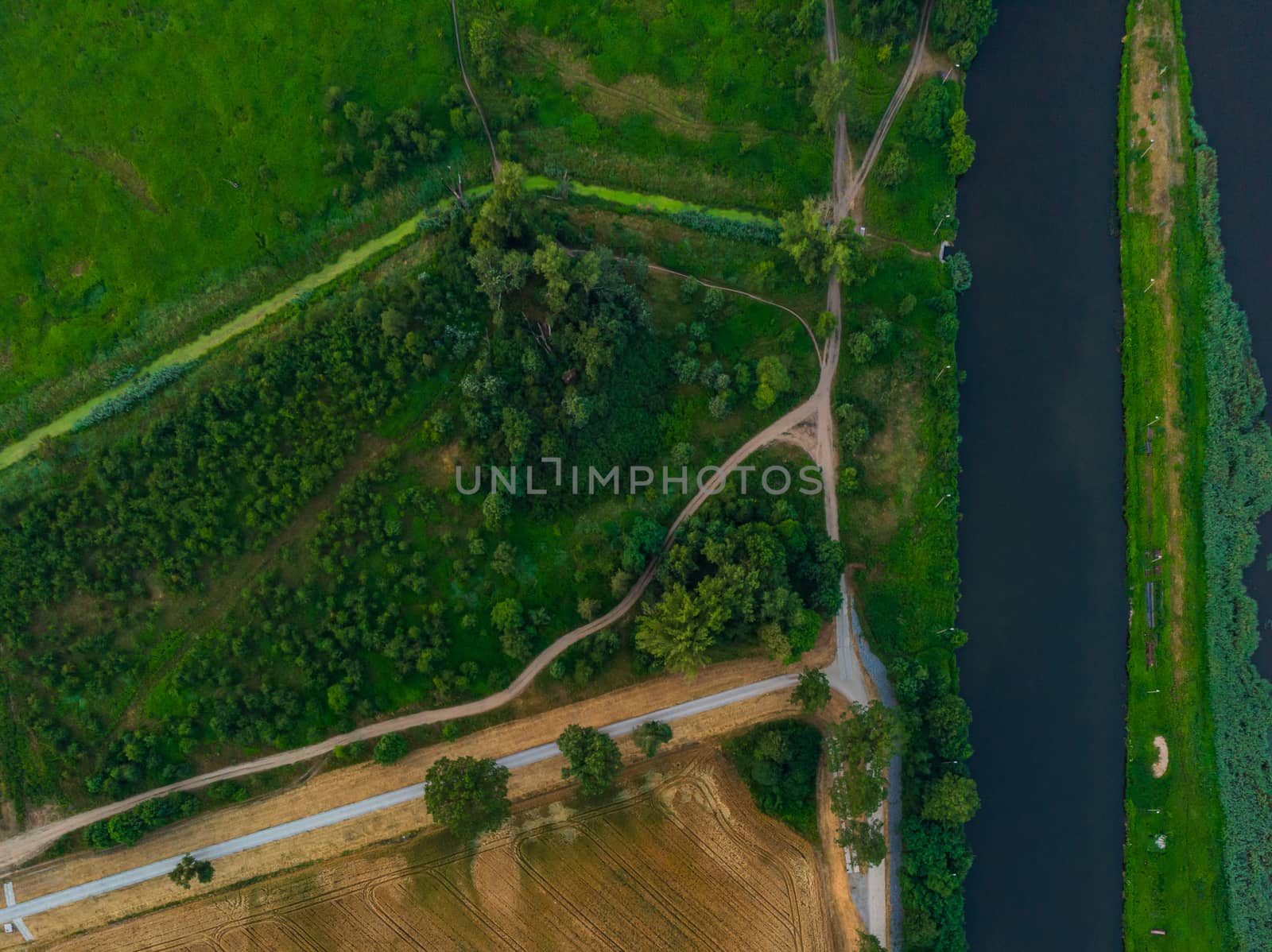 Aerial top down look to streets and paths between forest and fields and river on side