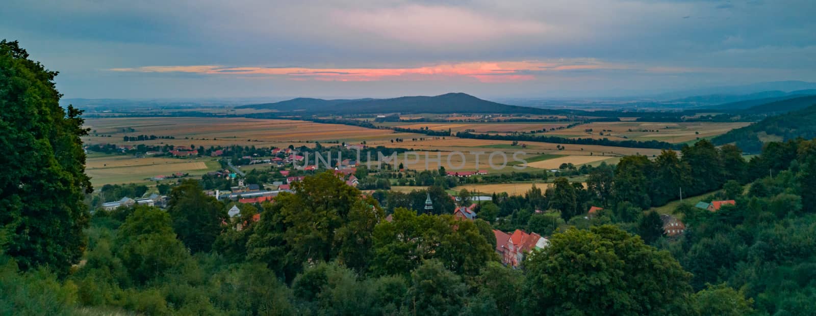 Panorama of red sunset between clouds over fields mountains and small village