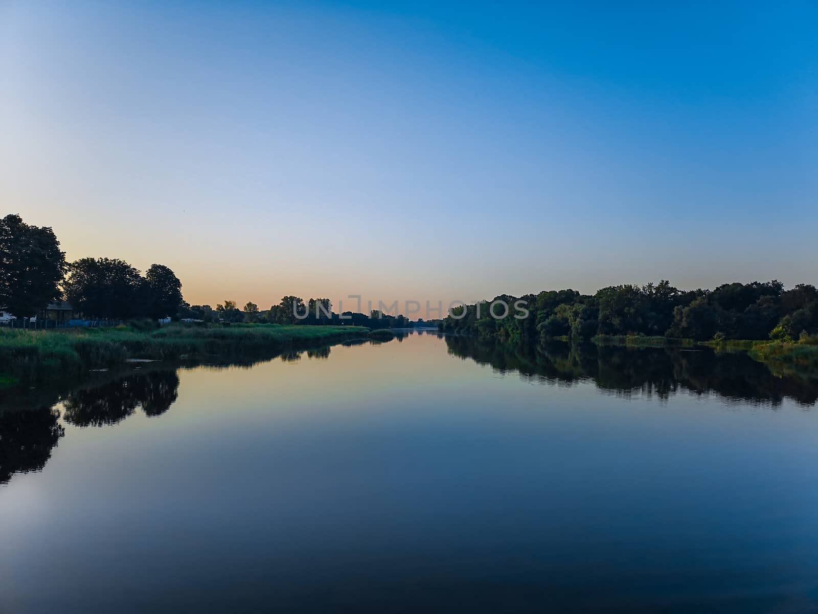 Long river without waves between trees at sunny morning