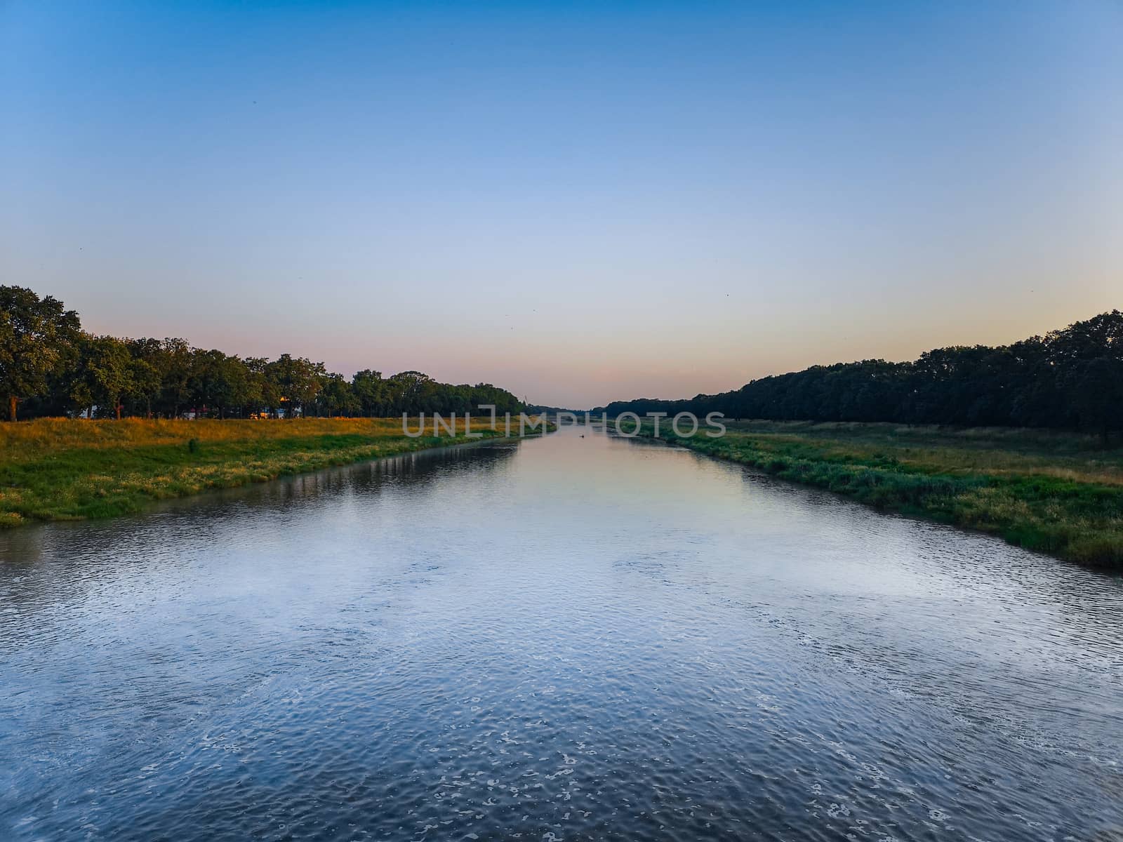 Long river with waves between trees at sunny morning