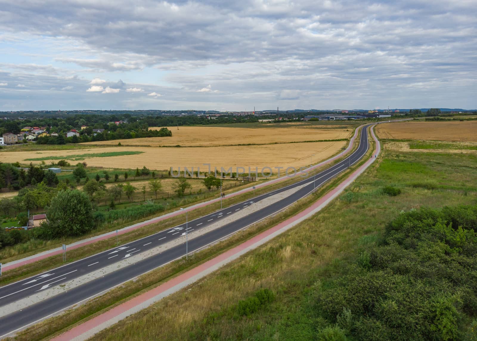 Aerial view of Long highway between yellow wheat fields at cloudy day by Wierzchu