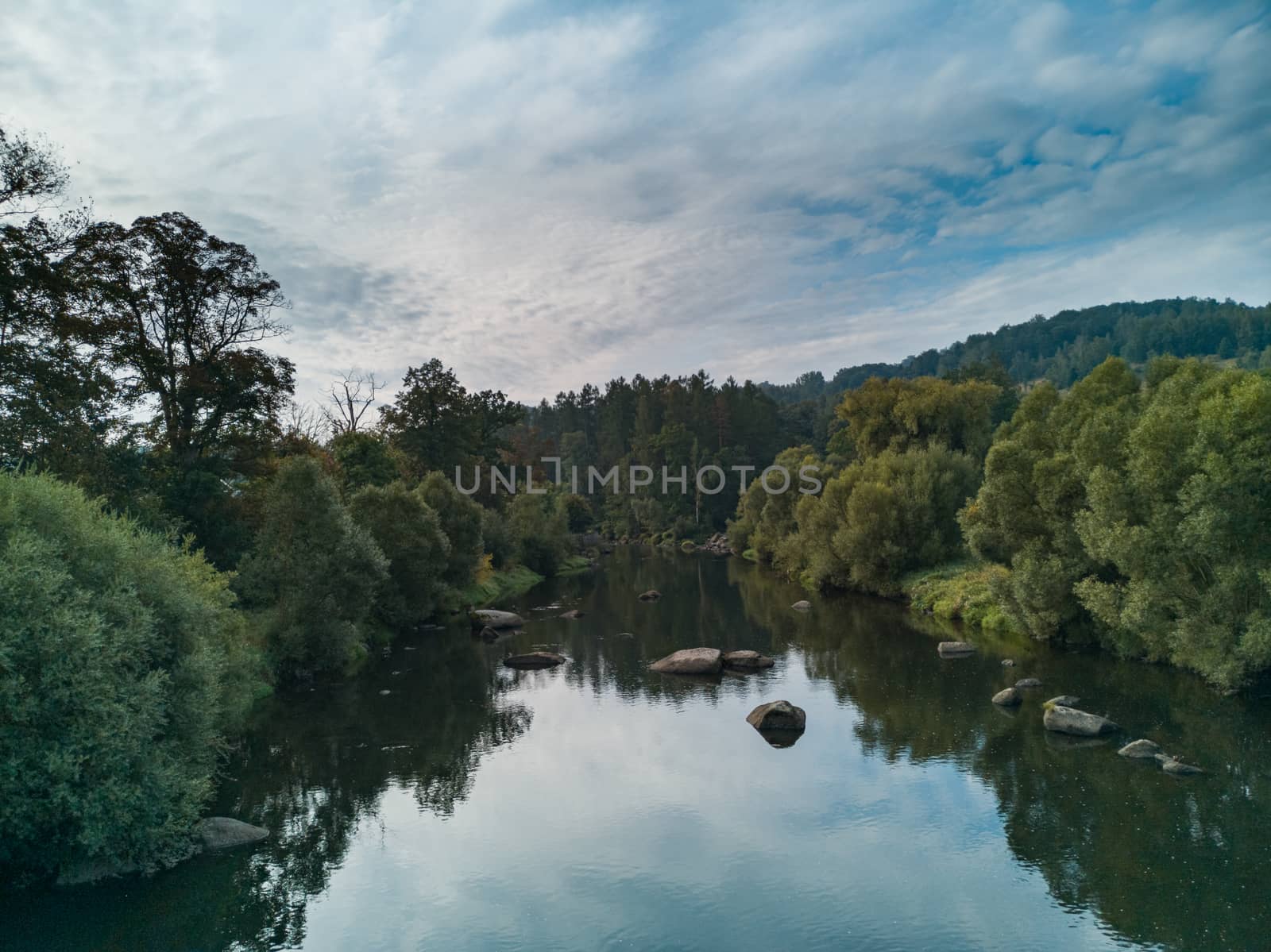 Colorful landscape with small river full of large stones between bushes and trees at cloudy morning by Wierzchu