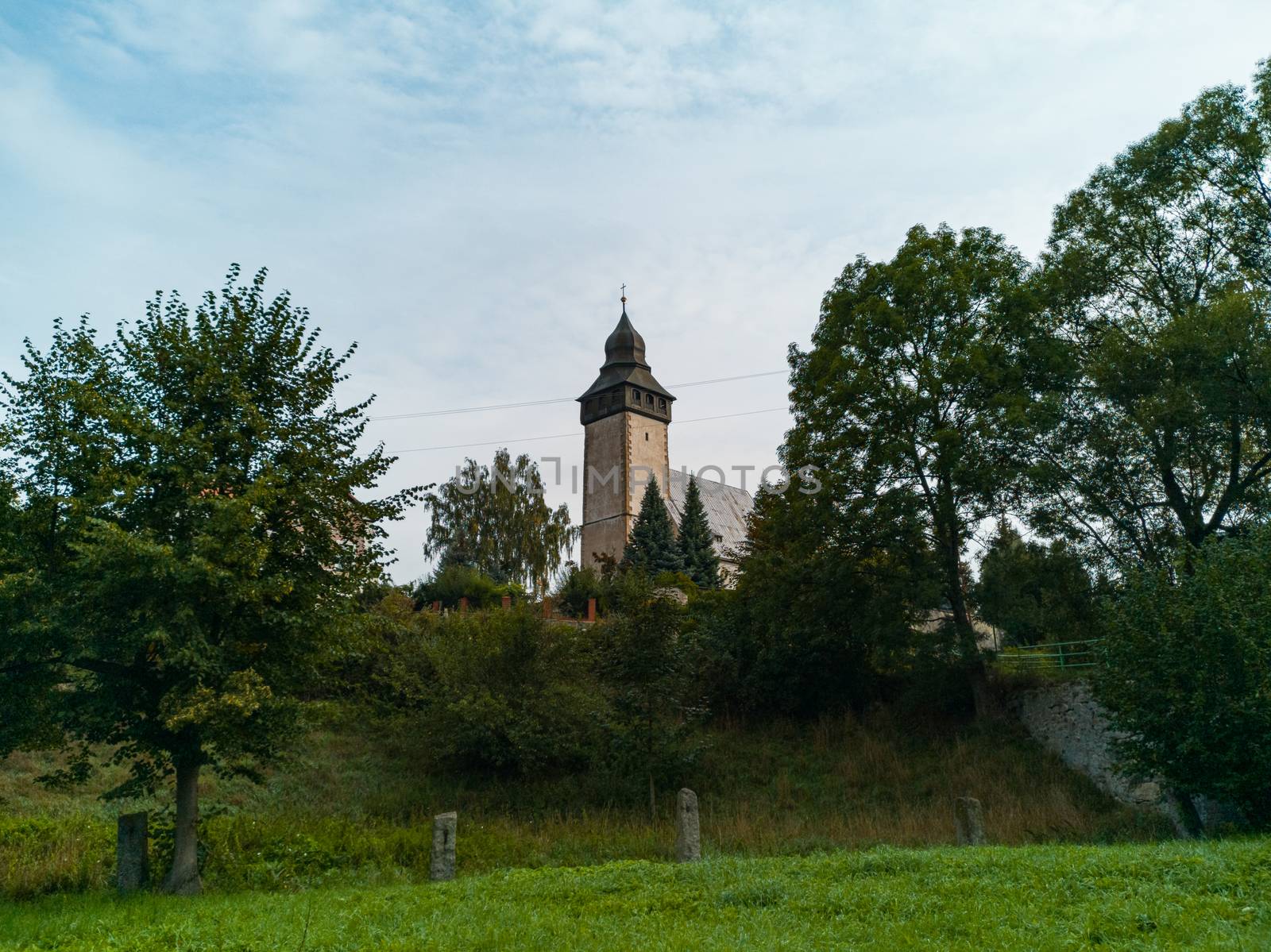 Small church with big tower behind park in small village by Wierzchu