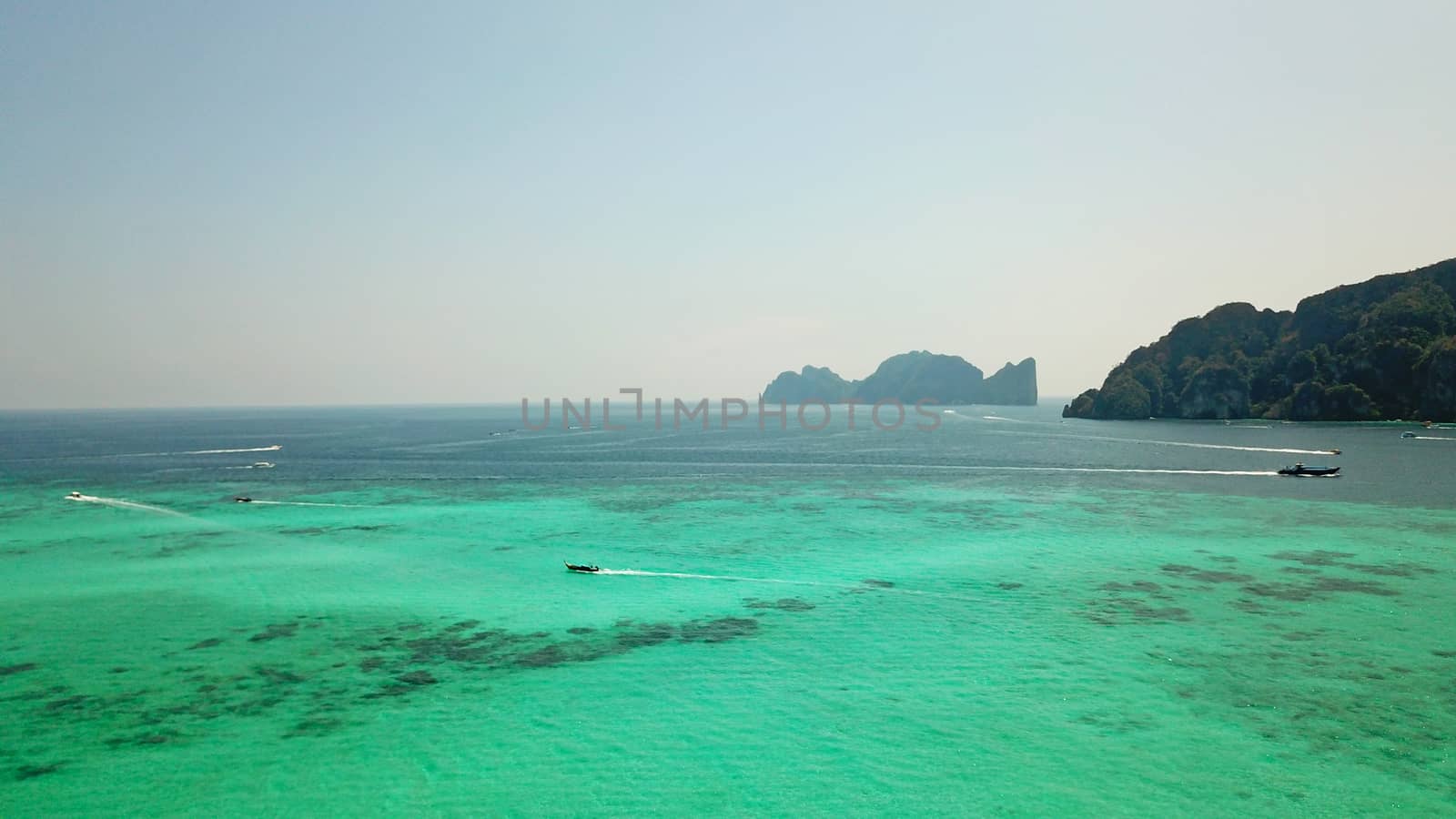 Turquoise clear water. Yachts, boats floating. Water Gradient from light to dark blue. Phi Phi don island, shooting from a drone from the air. White sand, green trees, palm trees and large hills.