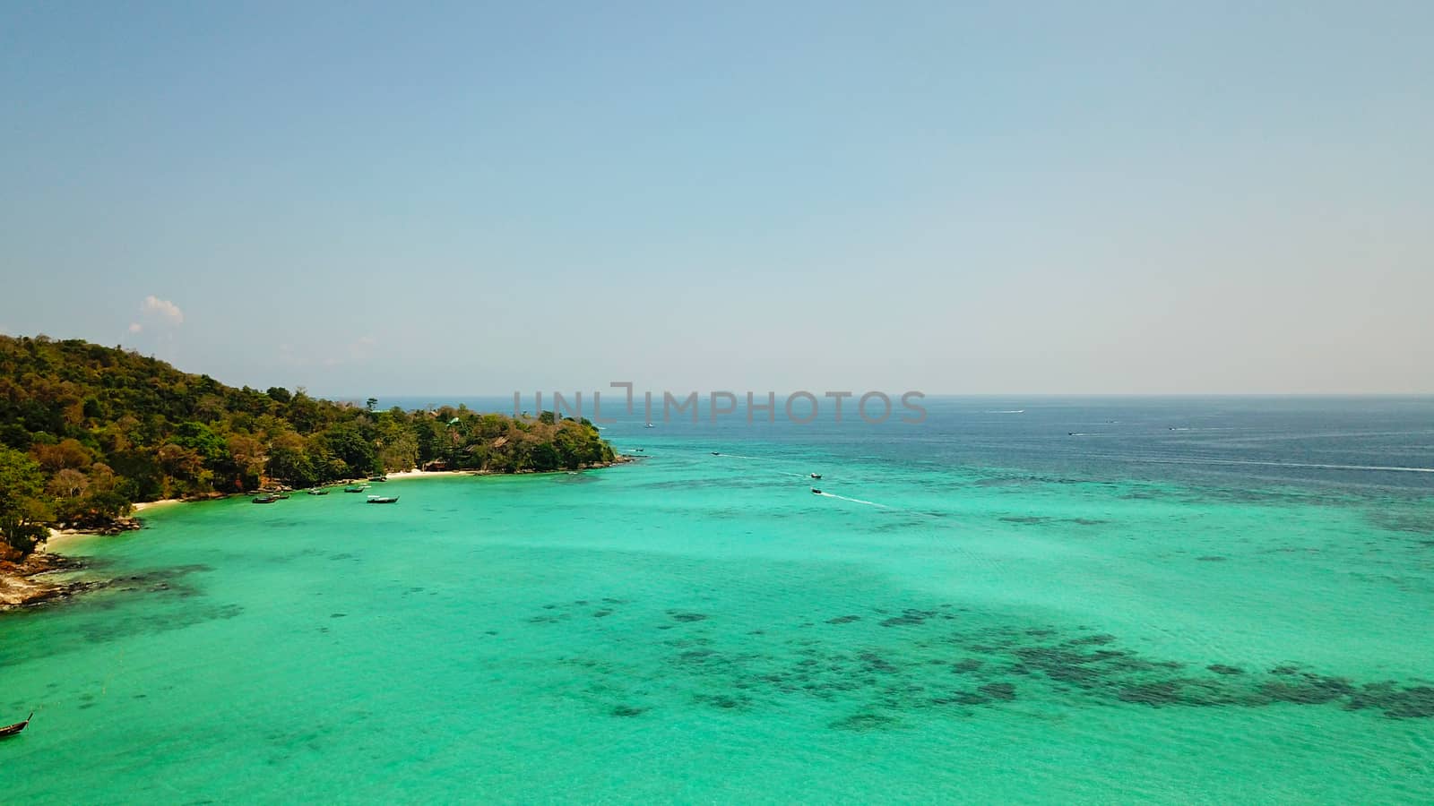 Turquoise clear water. Yachts, boats floating. Water Gradient from light to dark blue. Phi Phi don island, shooting from a drone from the air. White sand, green trees, palm trees and large hills.