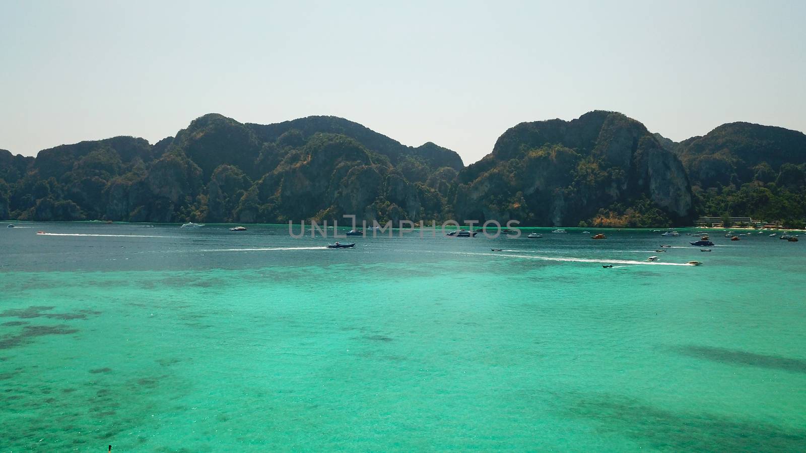 Turquoise clear water. Yachts, boats floating. Water Gradient from light to dark blue. Phi Phi don island, shooting from a drone from the air. White sand, green trees, palm trees and large hills.