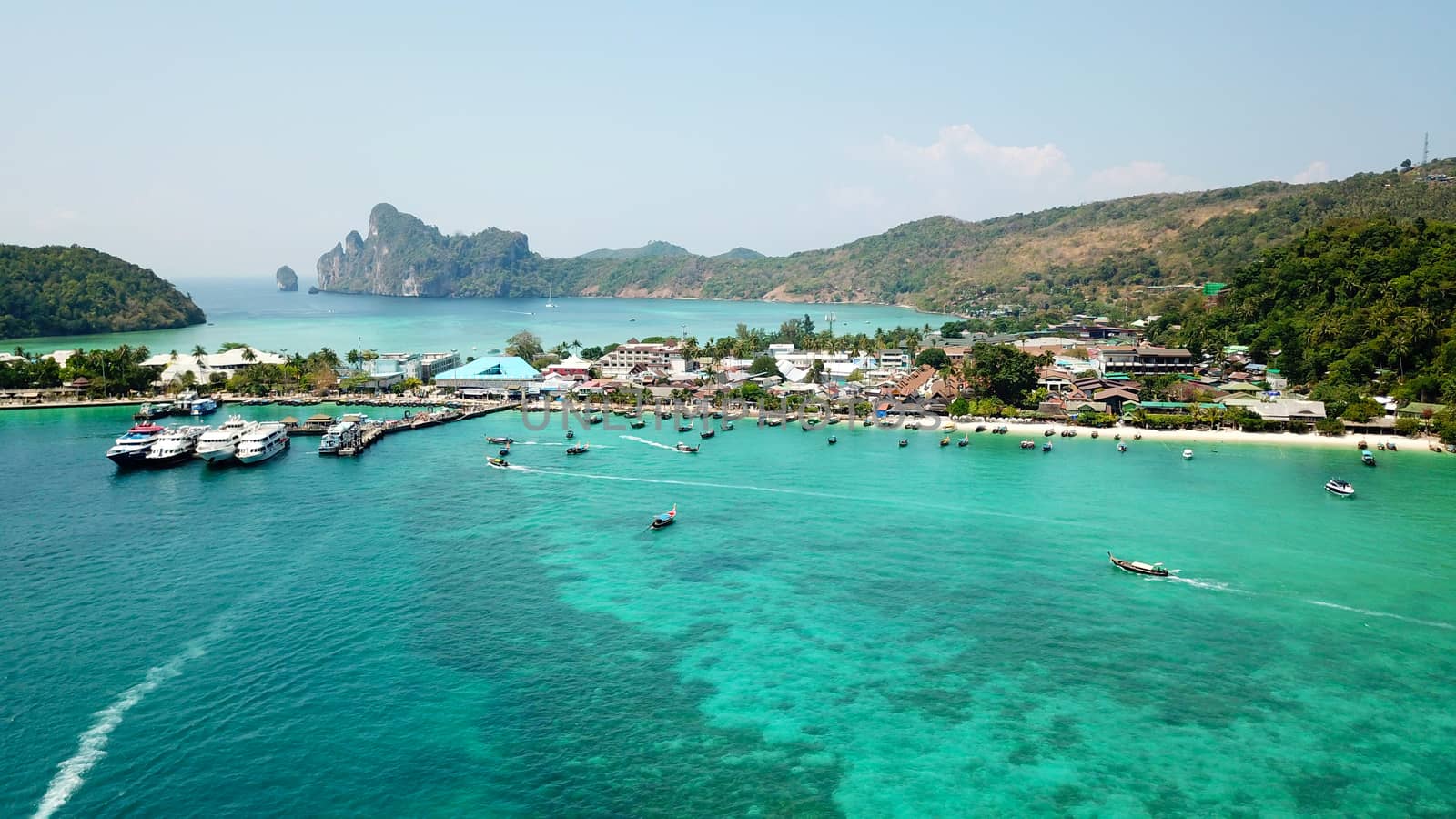 Turquoise clear water. Yachts, boats floating. Water Gradient from light to dark blue. Phi Phi don island, shooting from a drone from the air. White sand, green trees, palm trees and large hills.