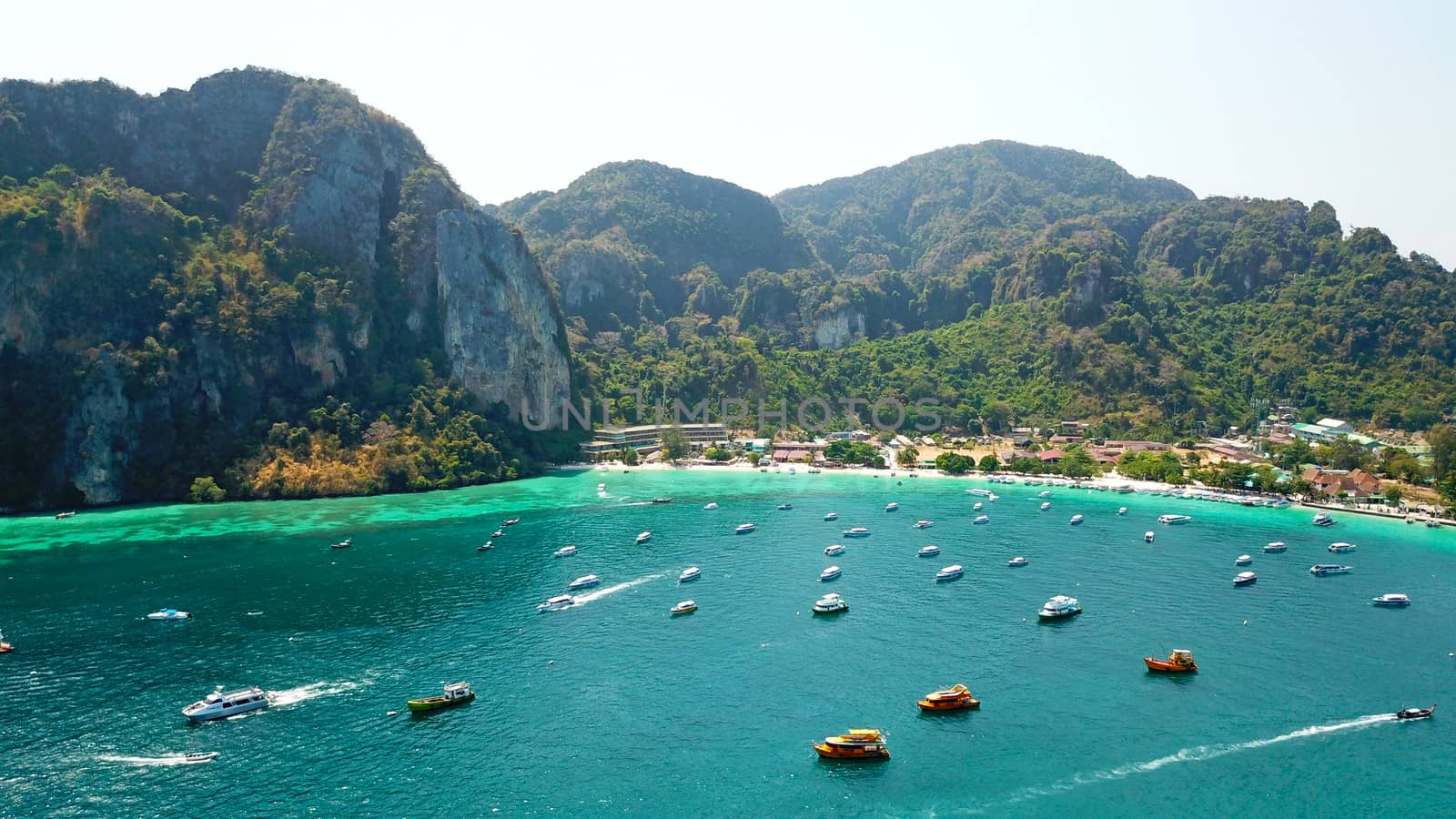 Turquoise clear water. Yachts, boats floating. Water Gradient from light to dark blue. Phi Phi don island, shooting from a drone from the air. White sand, green trees, palm trees and large hills.