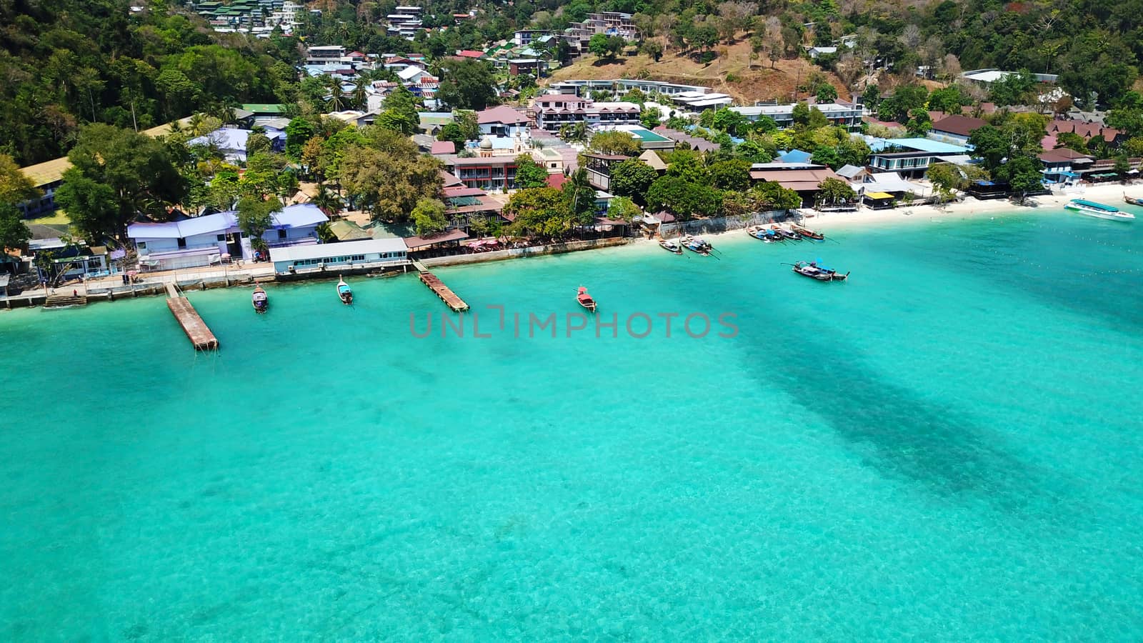 Turquoise clear water. Yachts, boats floating. Water Gradient from light to dark blue. Phi Phi don island, shooting from a drone from the air. White sand, green trees, palm trees and large hills.