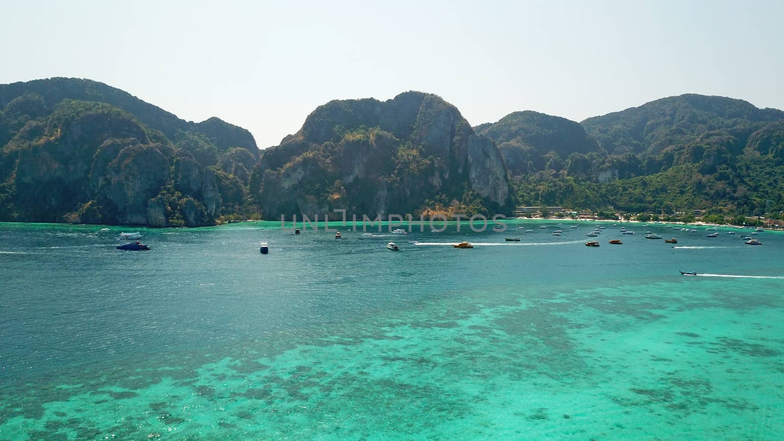 Turquoise clear water. Yachts, boats floating. Water Gradient from light to dark blue. Phi Phi don island, shooting from a drone from the air. White sand, green trees, palm trees and large hills.