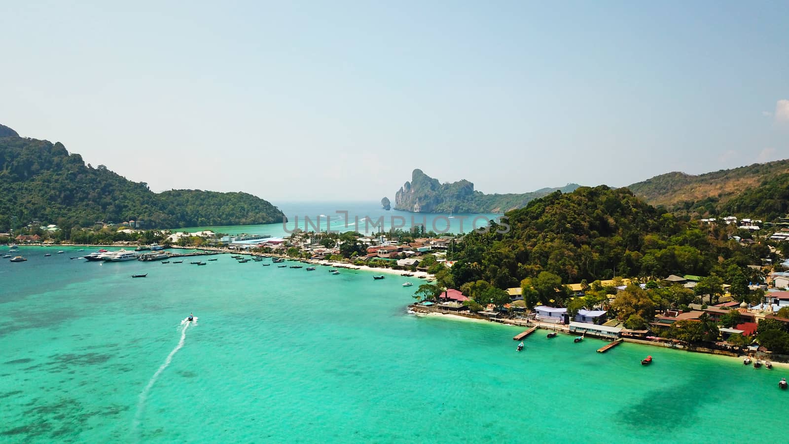 Turquoise clear water. Yachts, boats floating. Water Gradient from light to dark blue. Phi Phi don island, shooting from a drone from the air. White sand, green trees, palm trees and large hills.